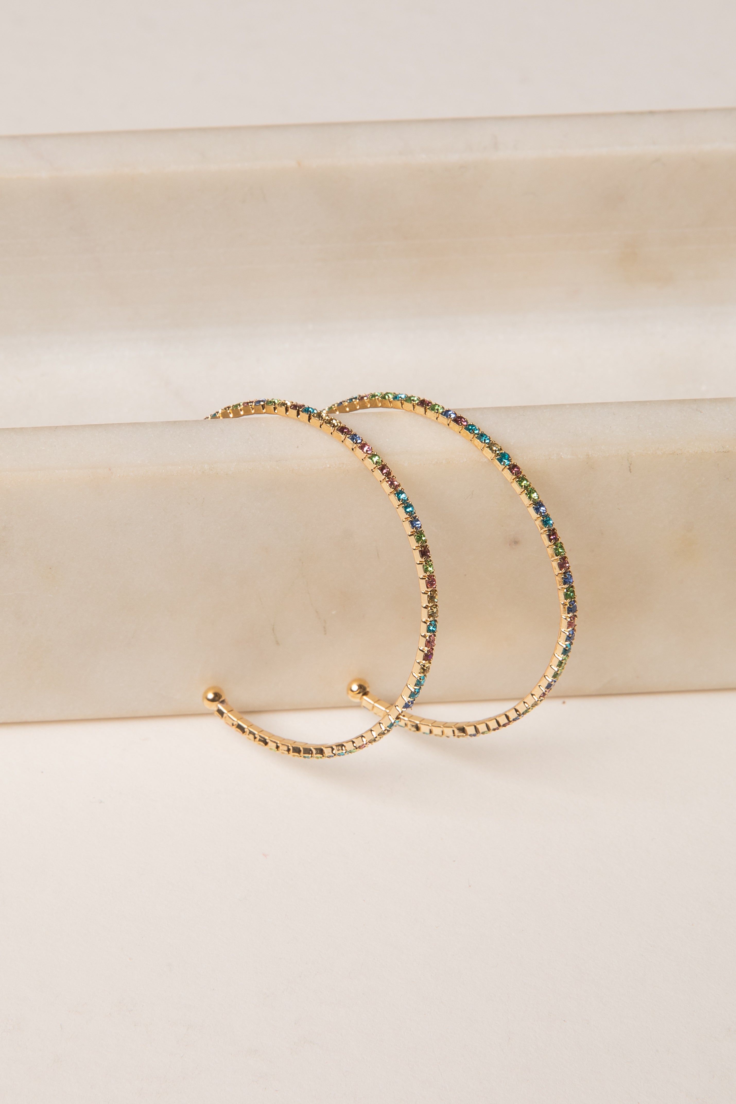Gold hoop earrings with multicolored beads on a beige surface