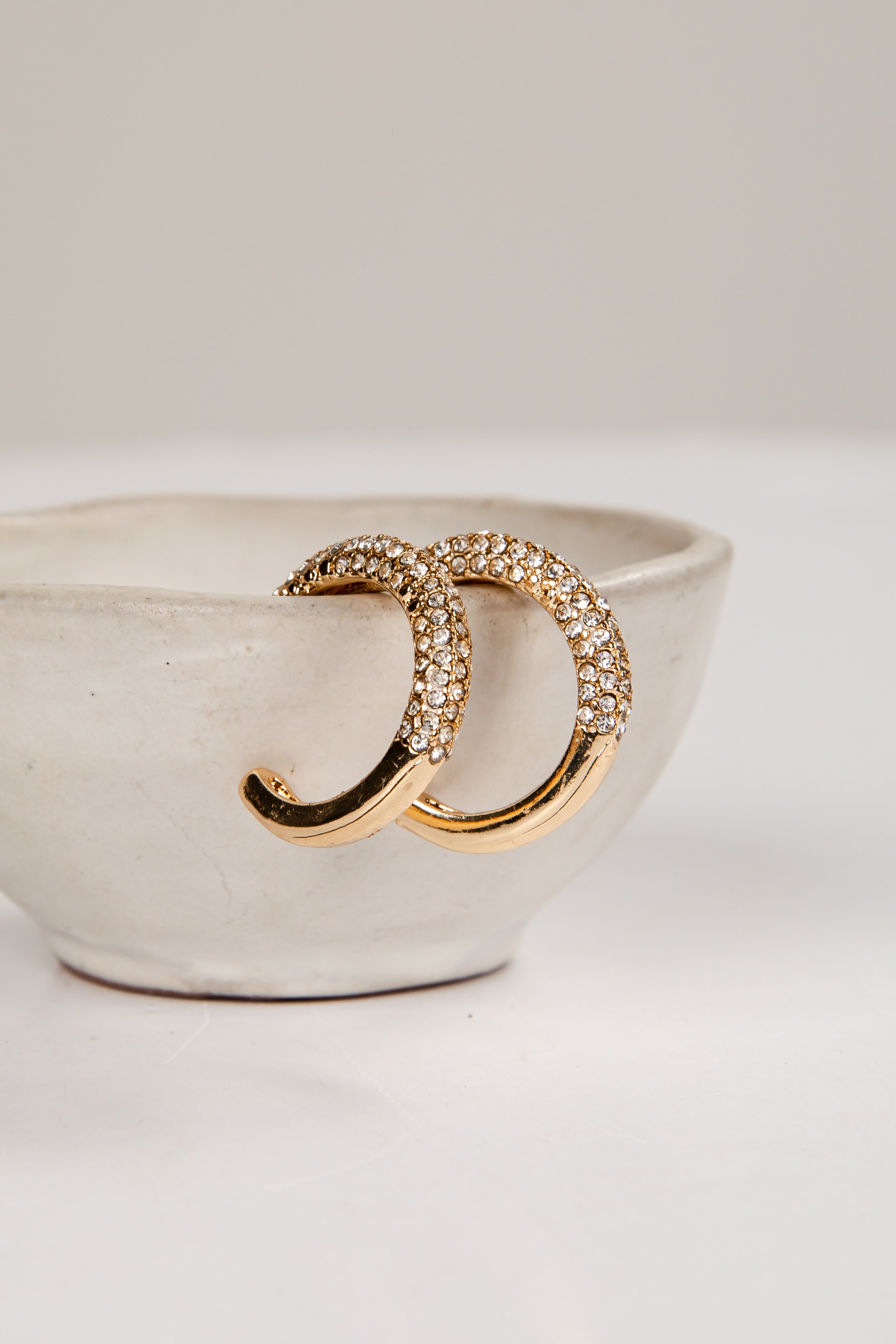 Gold hoop earrings with clear stones on a white dish