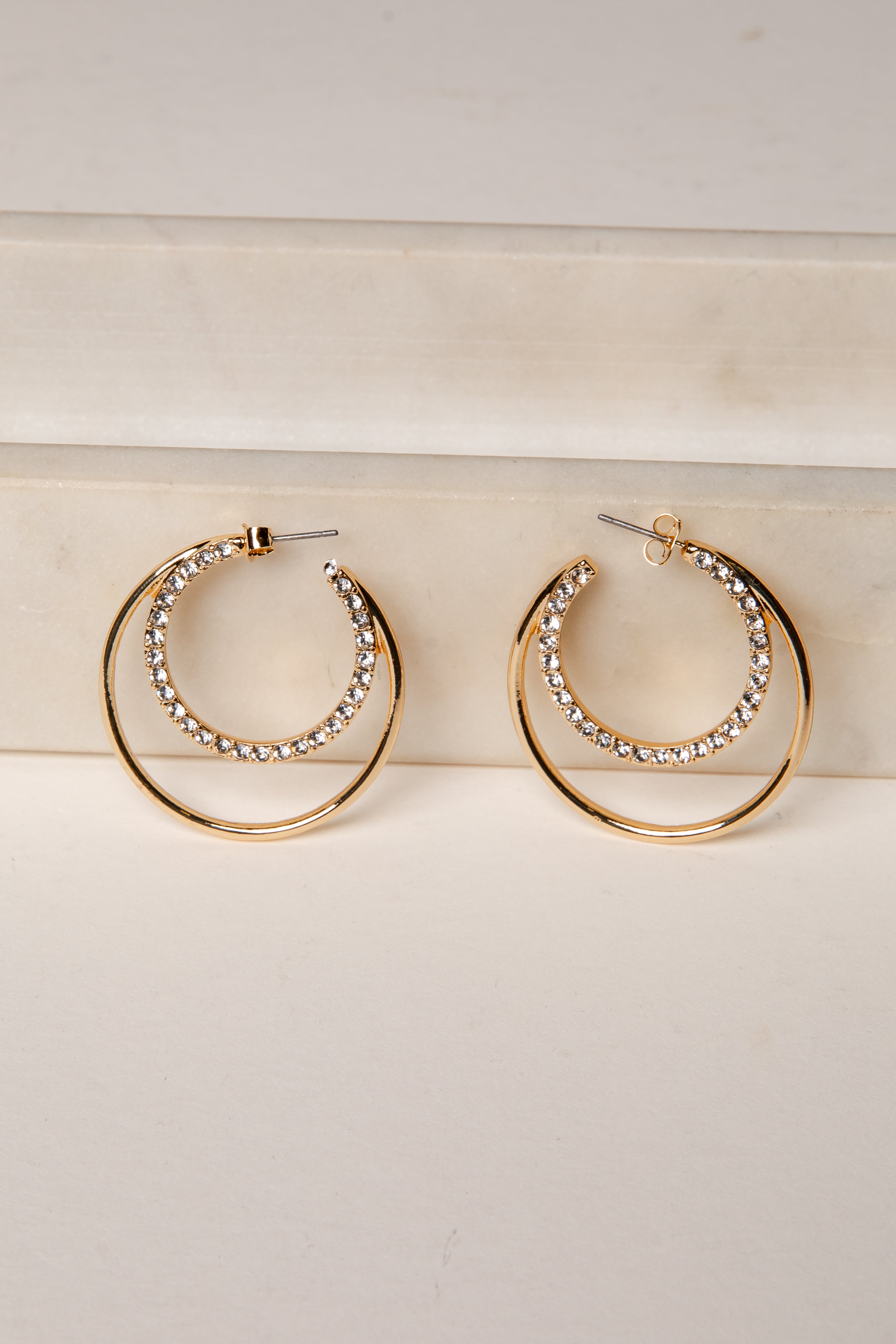 Gold hoop earrings with rhinestone detailing on a light wooden surface.