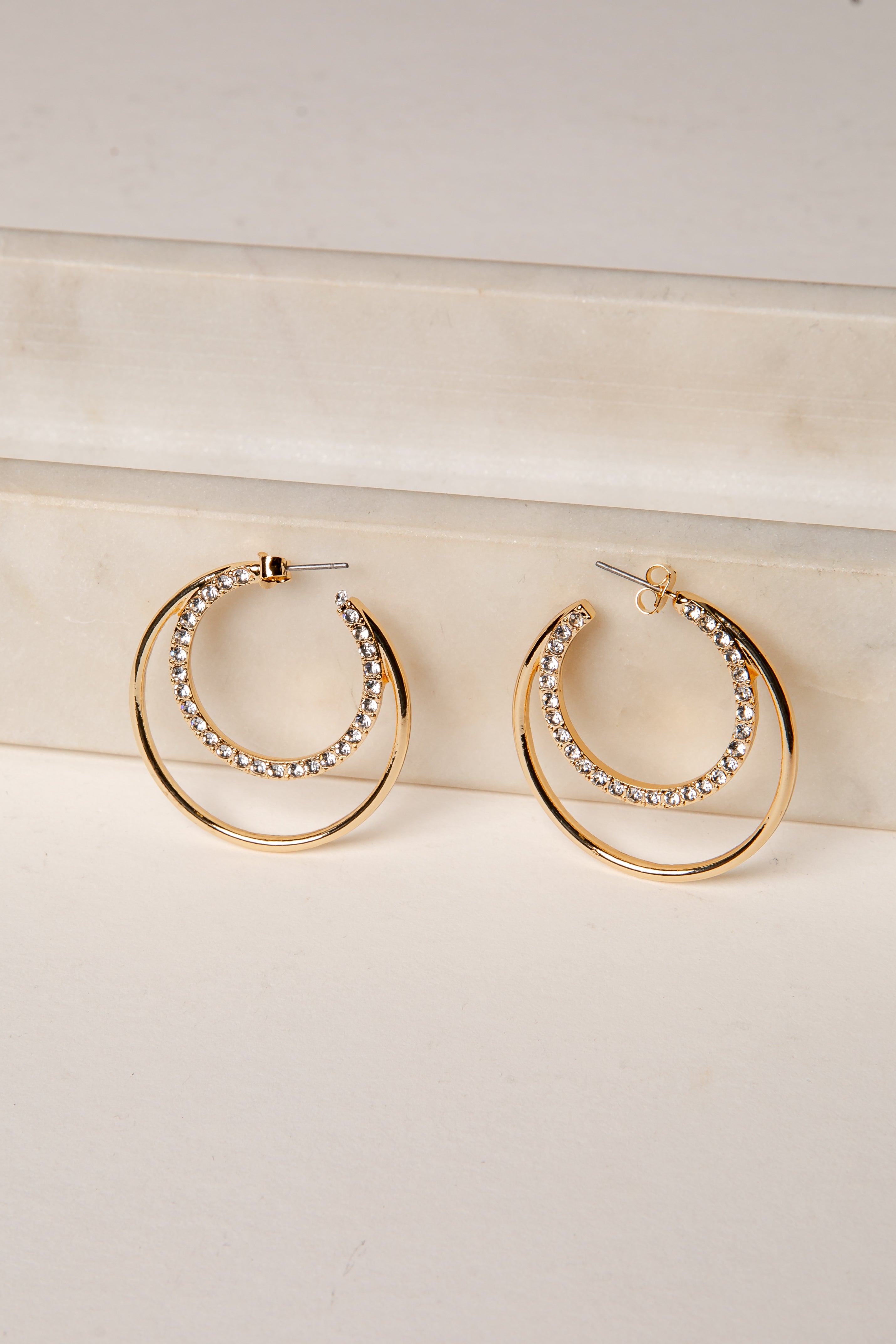 Gold hoop earrings with embedded stones on a light beige surface