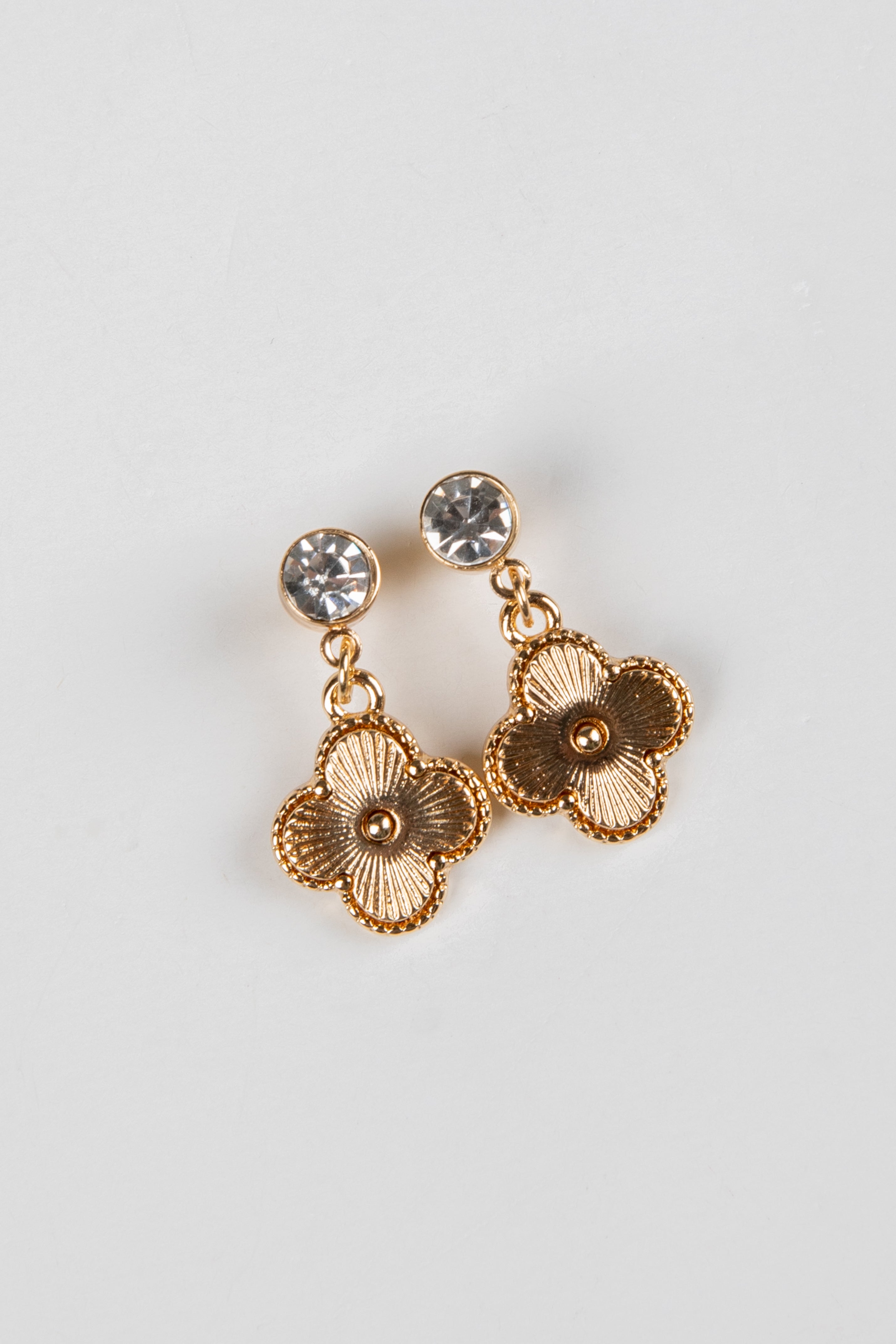 Gold floral earrings with clear gemstones on a light gray background