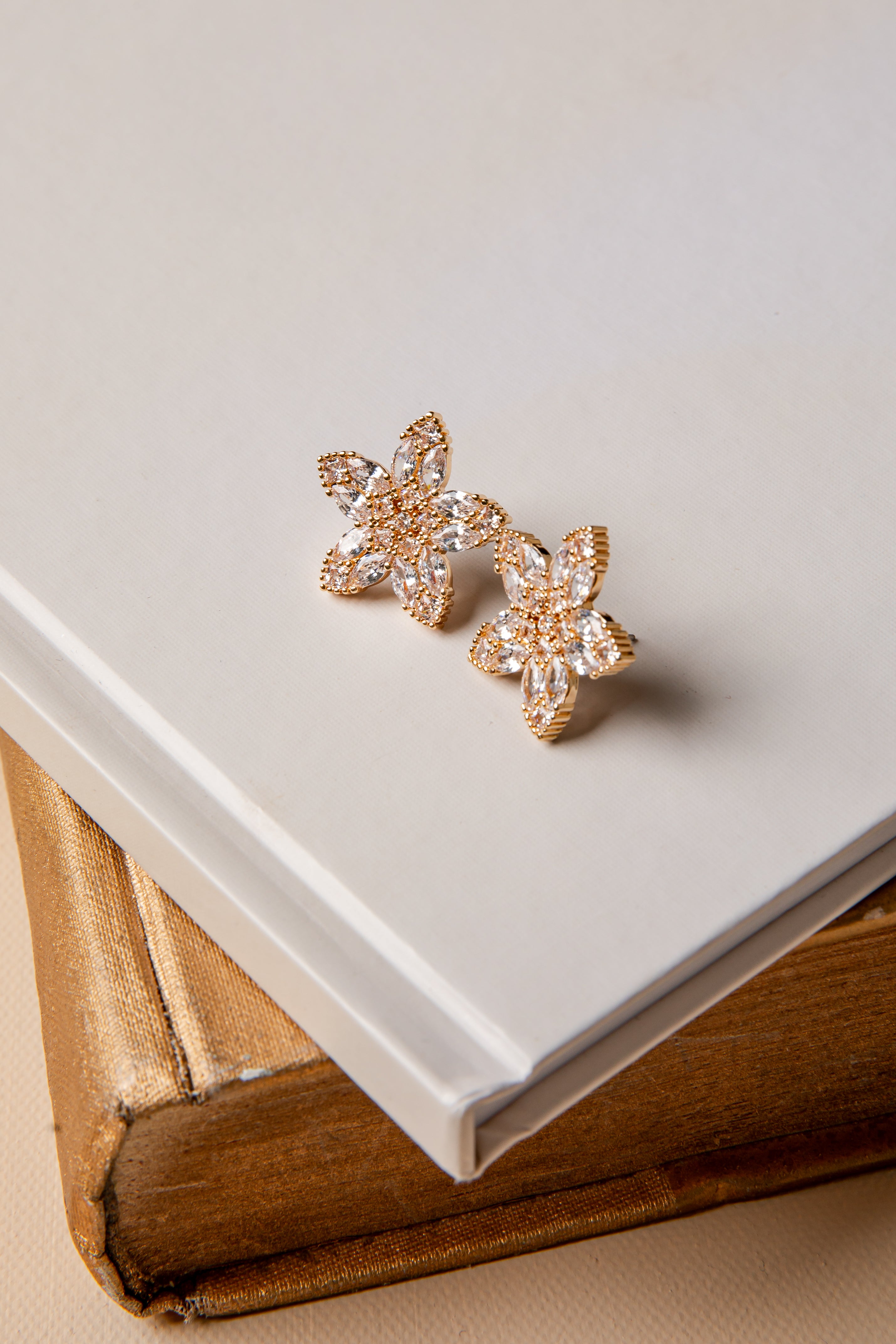 Gold flower earrings on a white surface with a book underneath