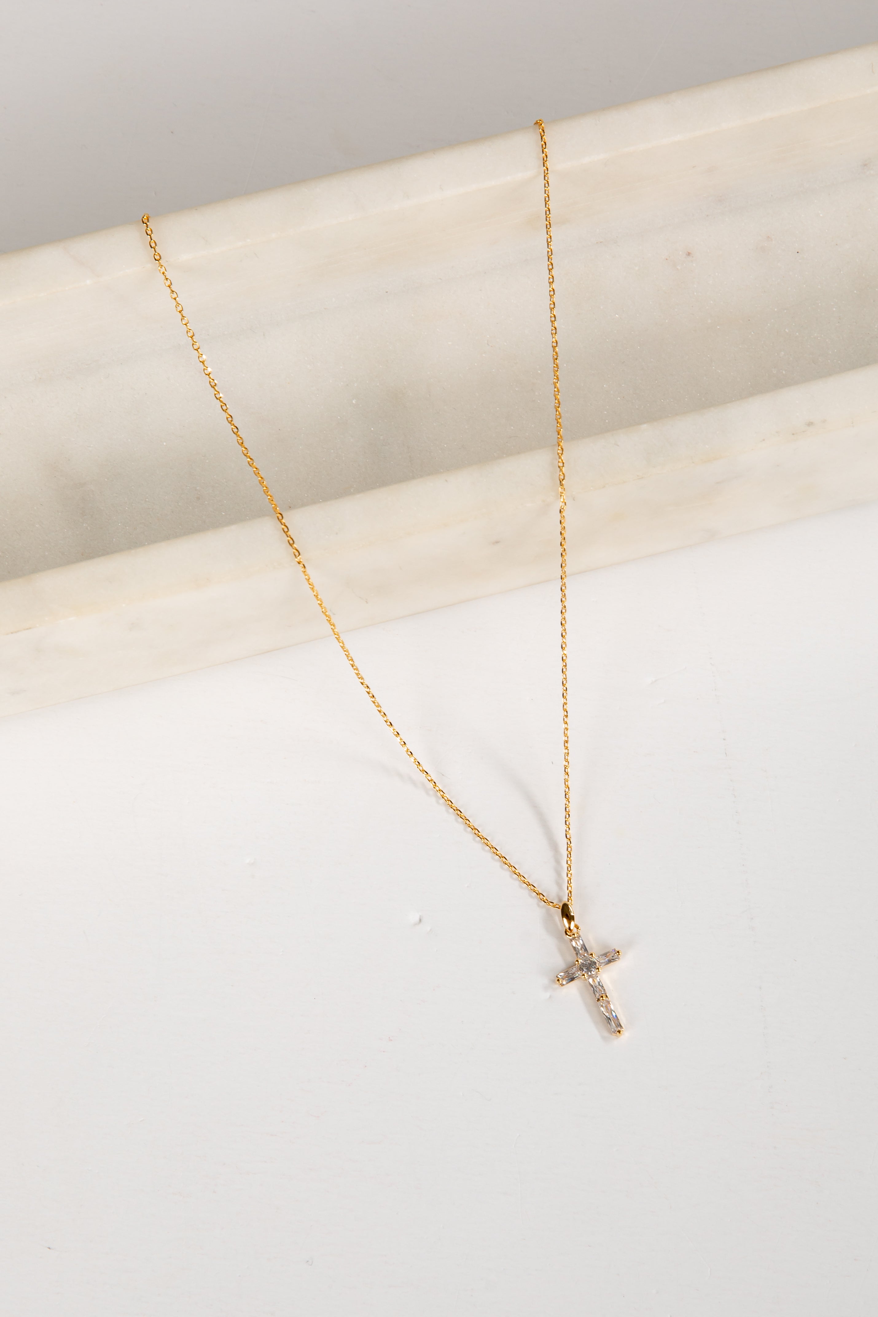 Gold necklace with a small cross pendant on a light background
