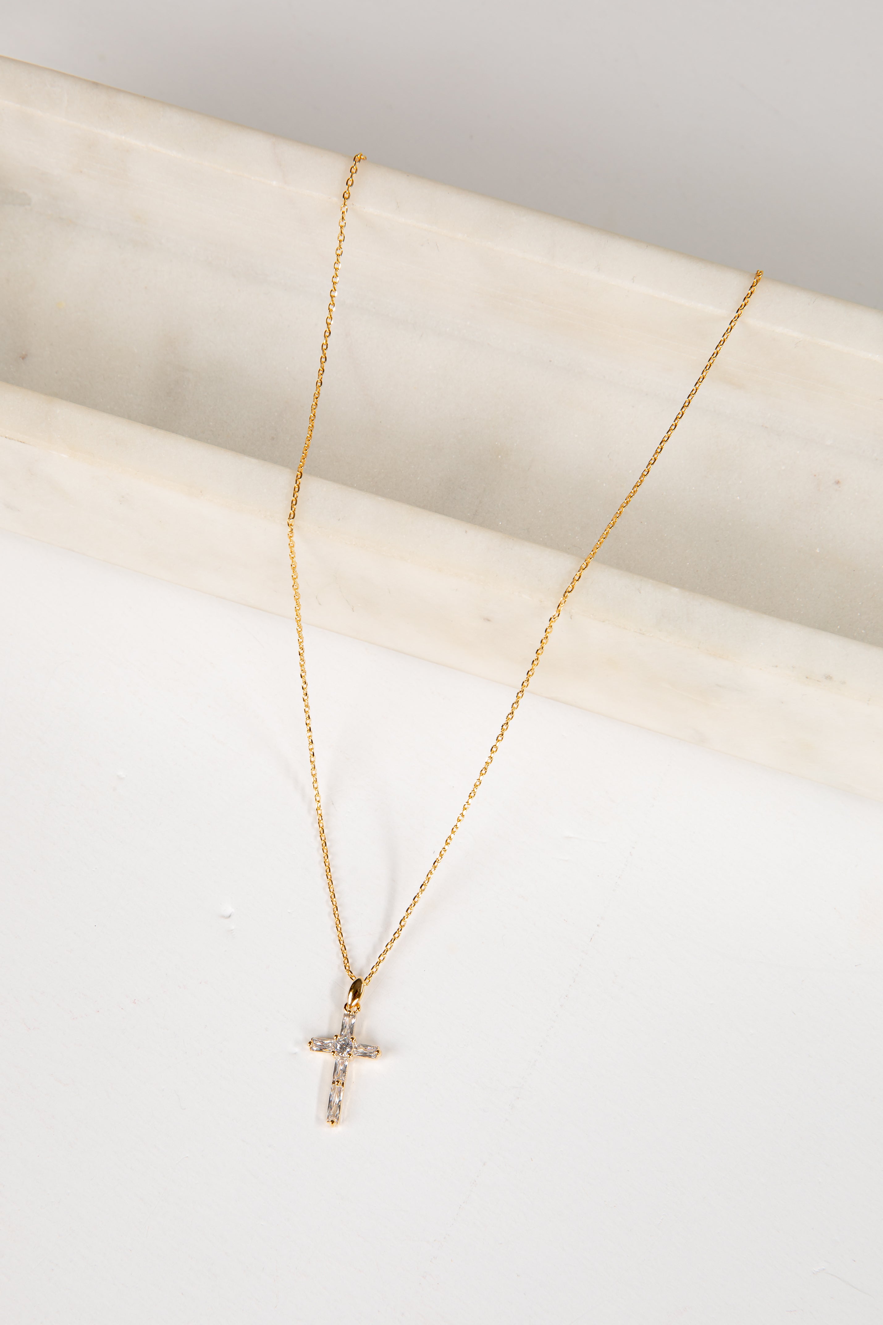 Gold necklace with a cross pendant on a light background
