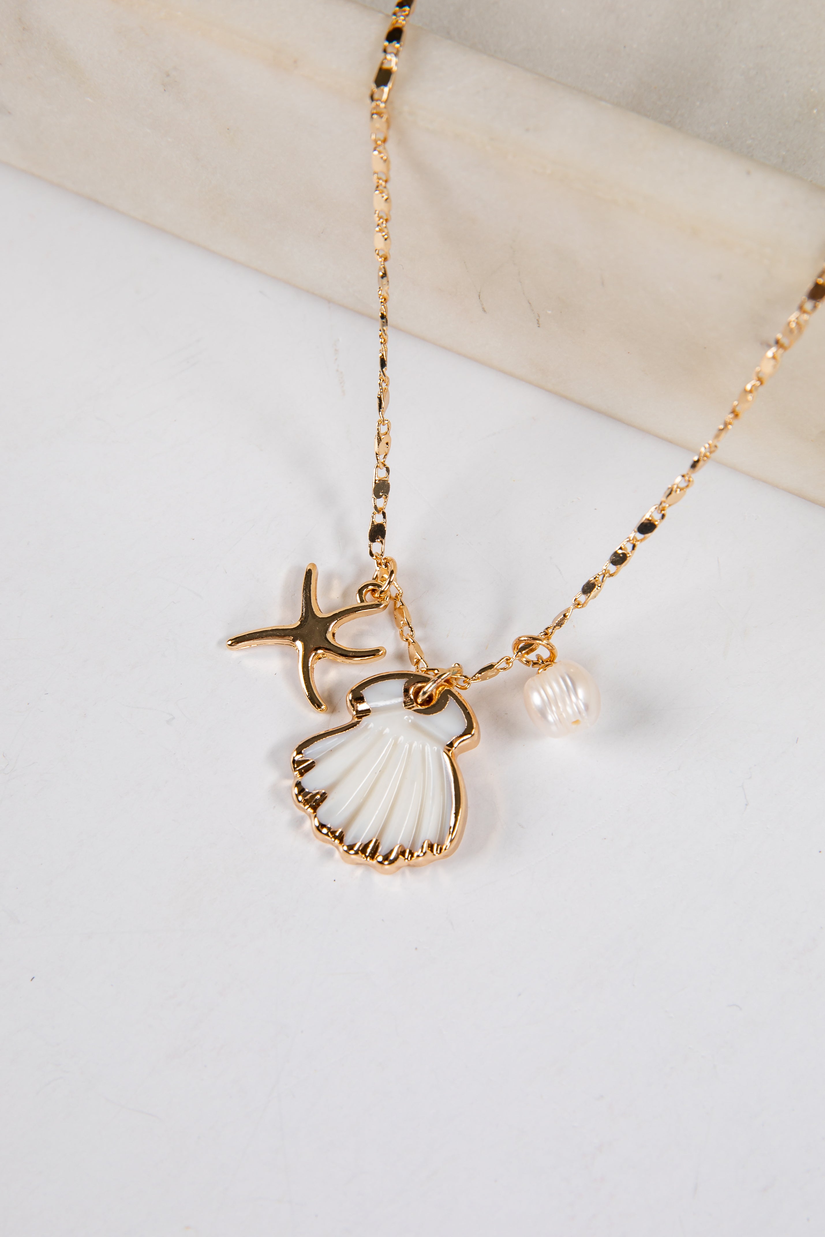 Gold necklace with shell and pearl pendant on a white surface
