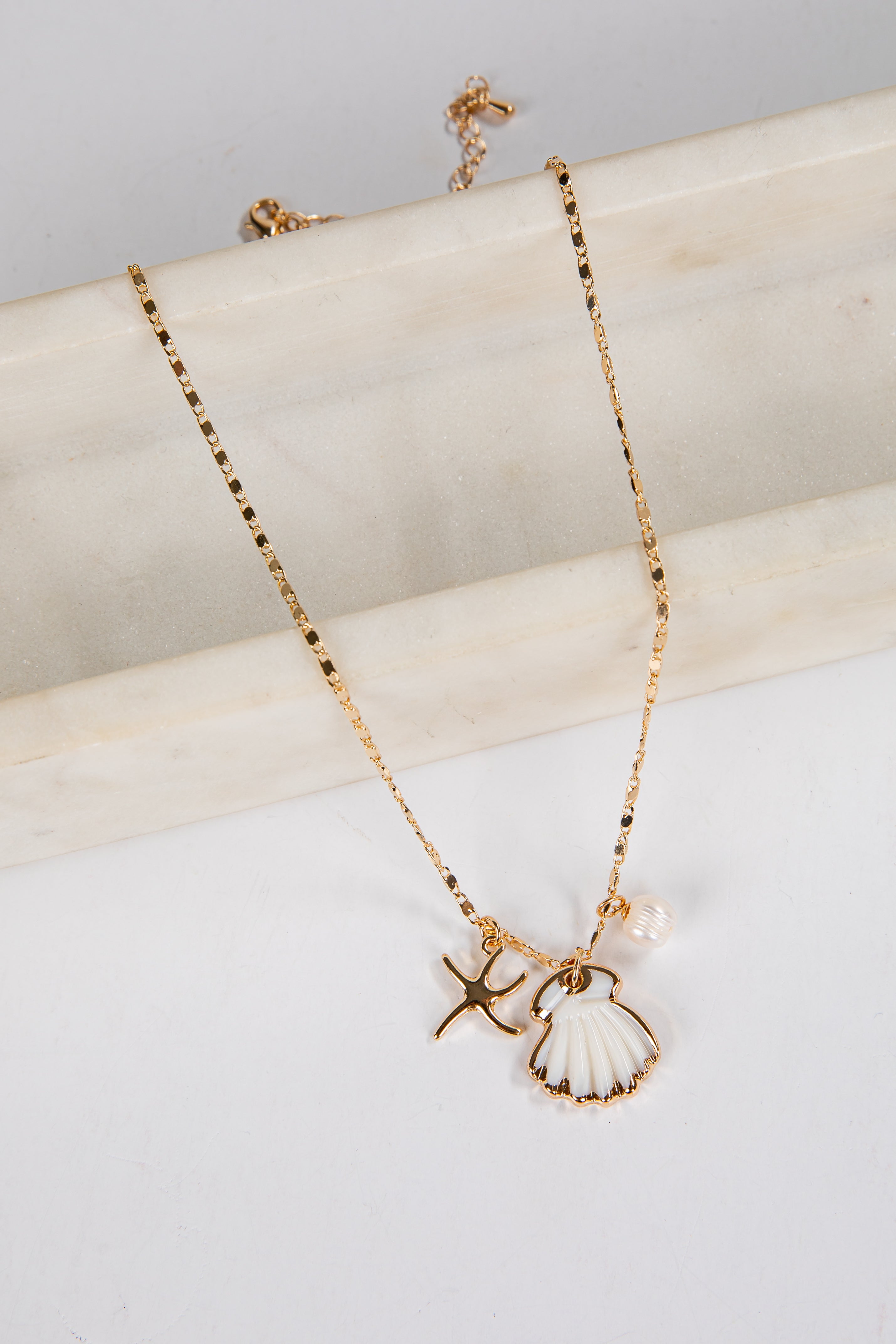 Gold necklace with shell and starfish charms on a marble surface