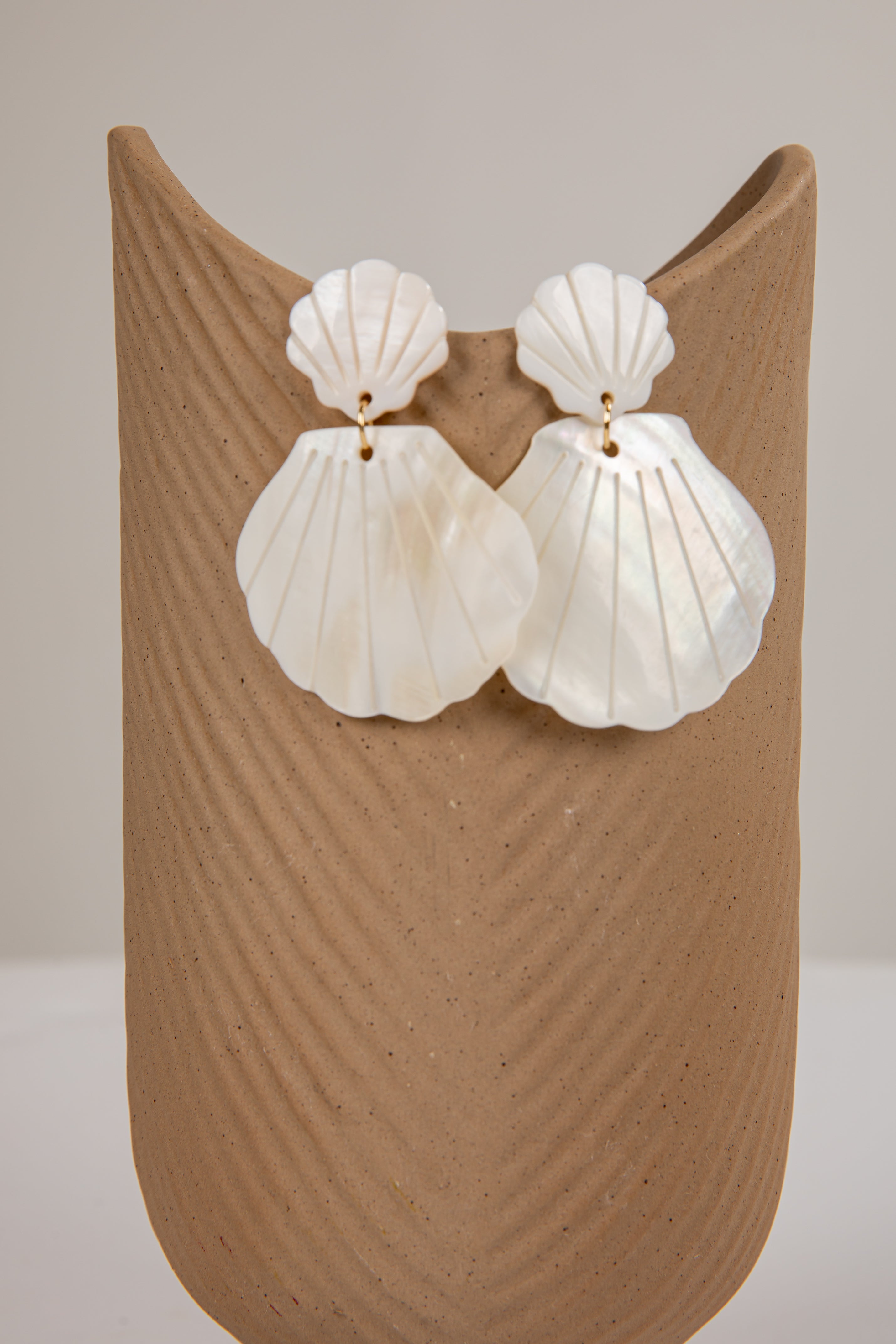 Shell-shaped earrings on a beige stand against a neutral background