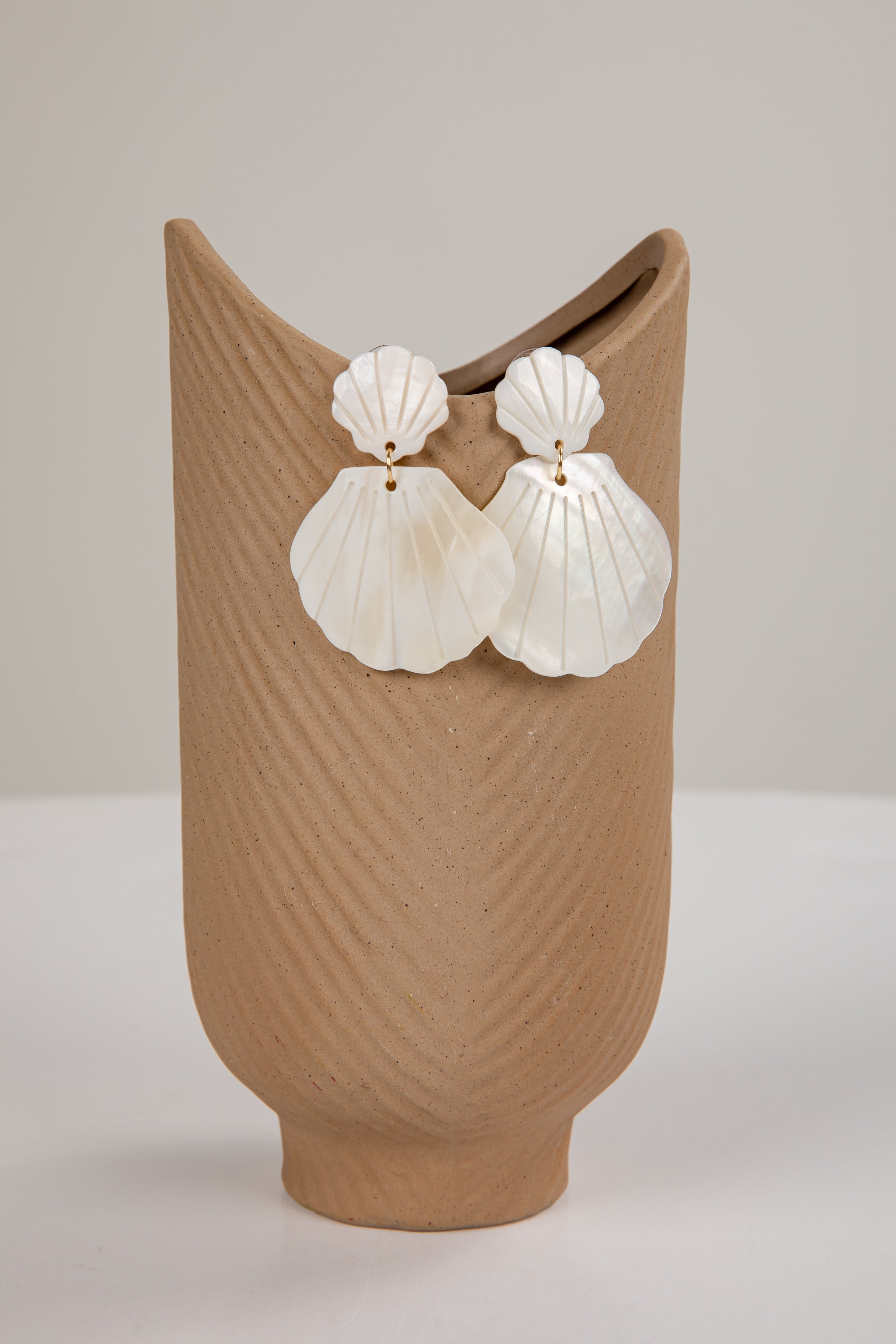 Shell-shaped earrings on a textured brown vase against a plain background
