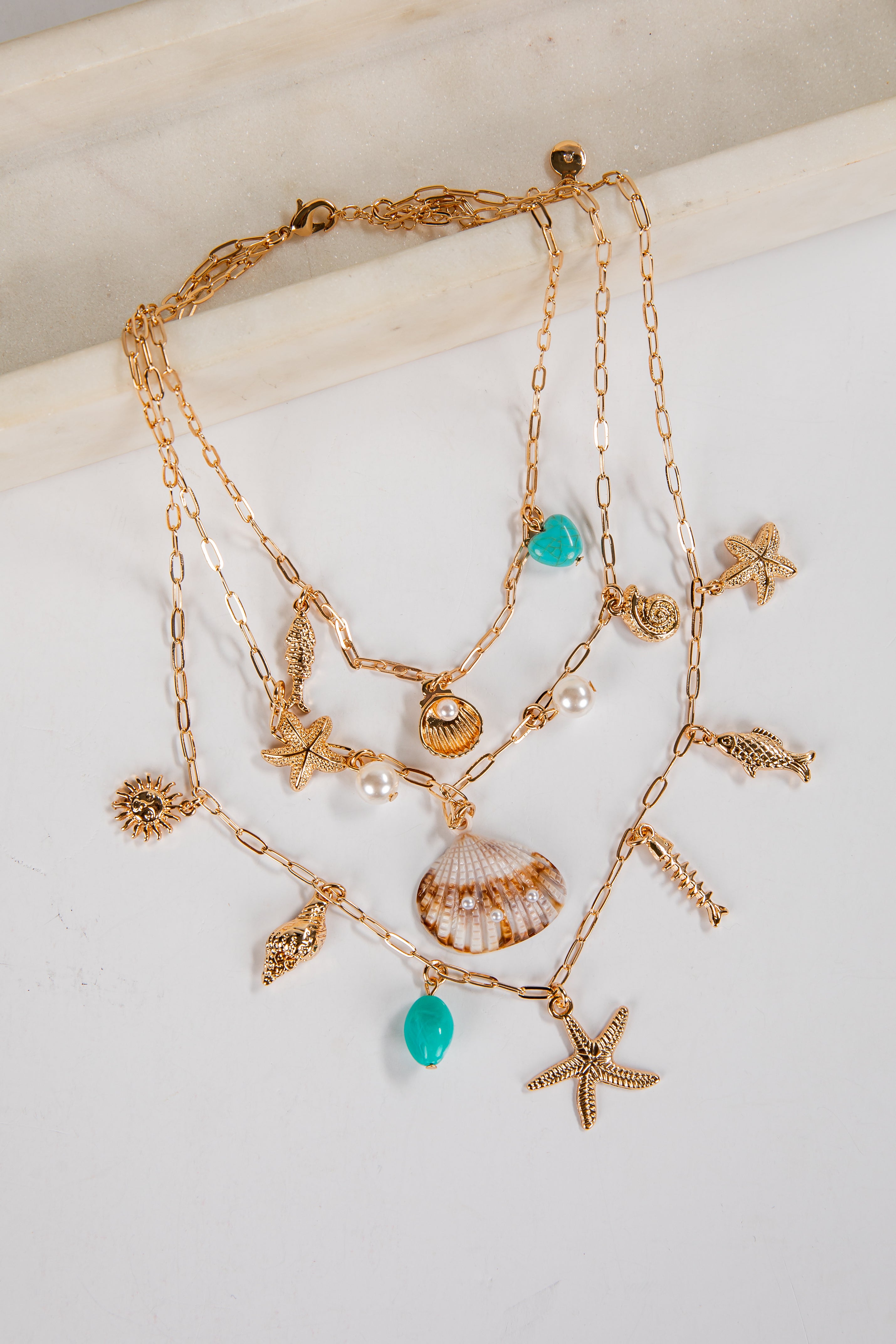 Gold necklace with starfish, shell, and turquoise bead charms on a white surface