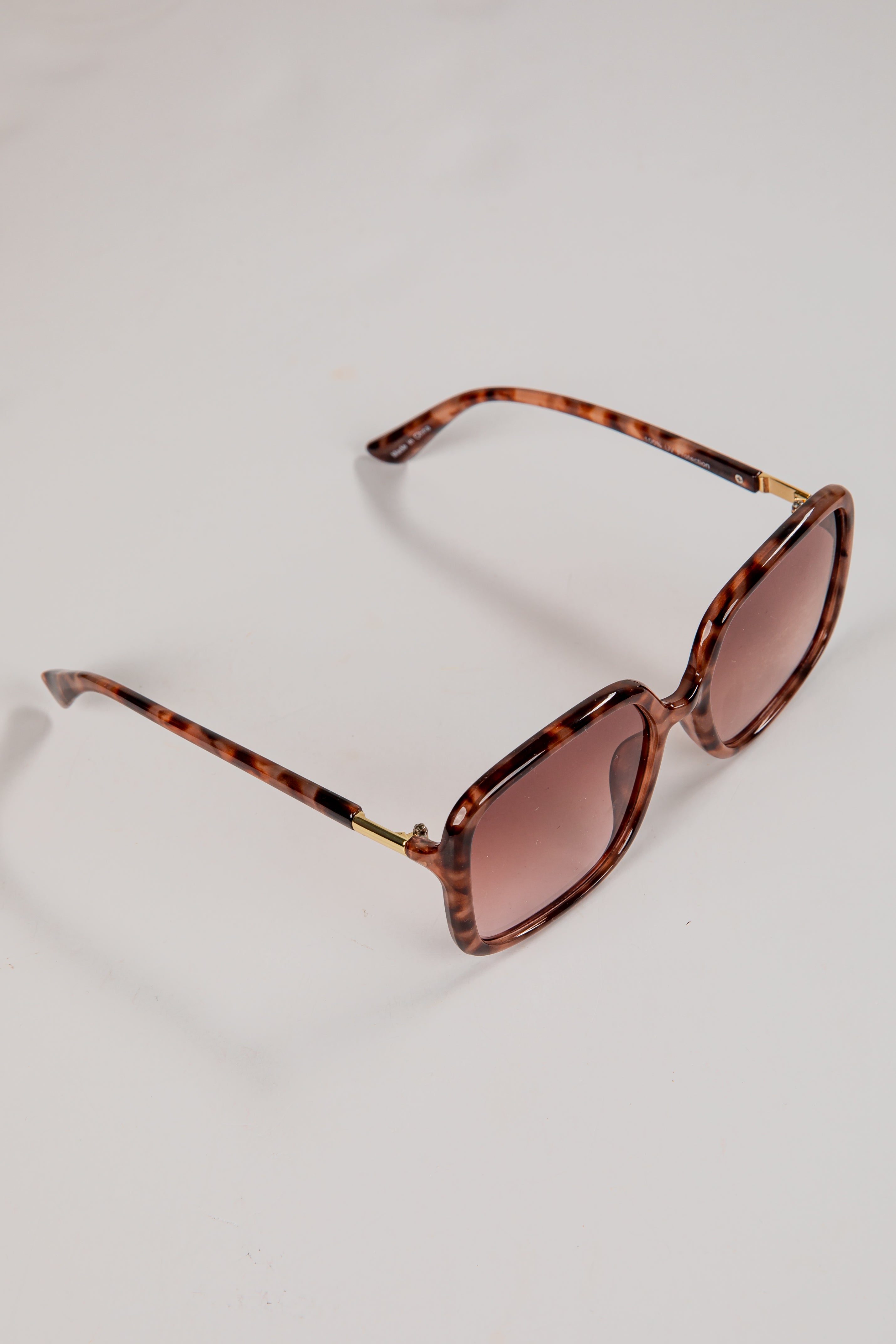Tortoiseshell sunglasses with brown lenses on a light gray background