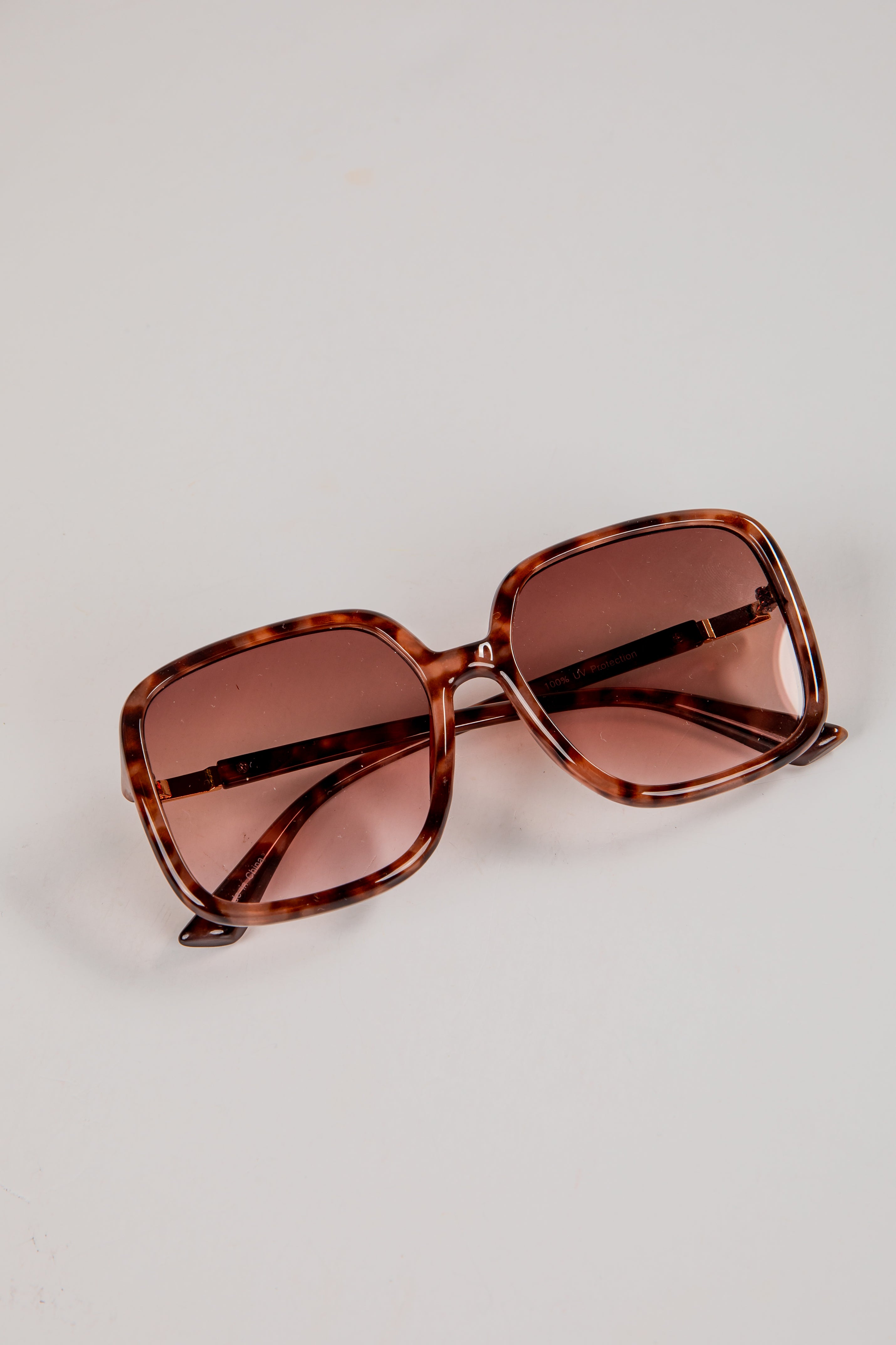 Brown sunglasses with tortoiseshell frame on a light gray background