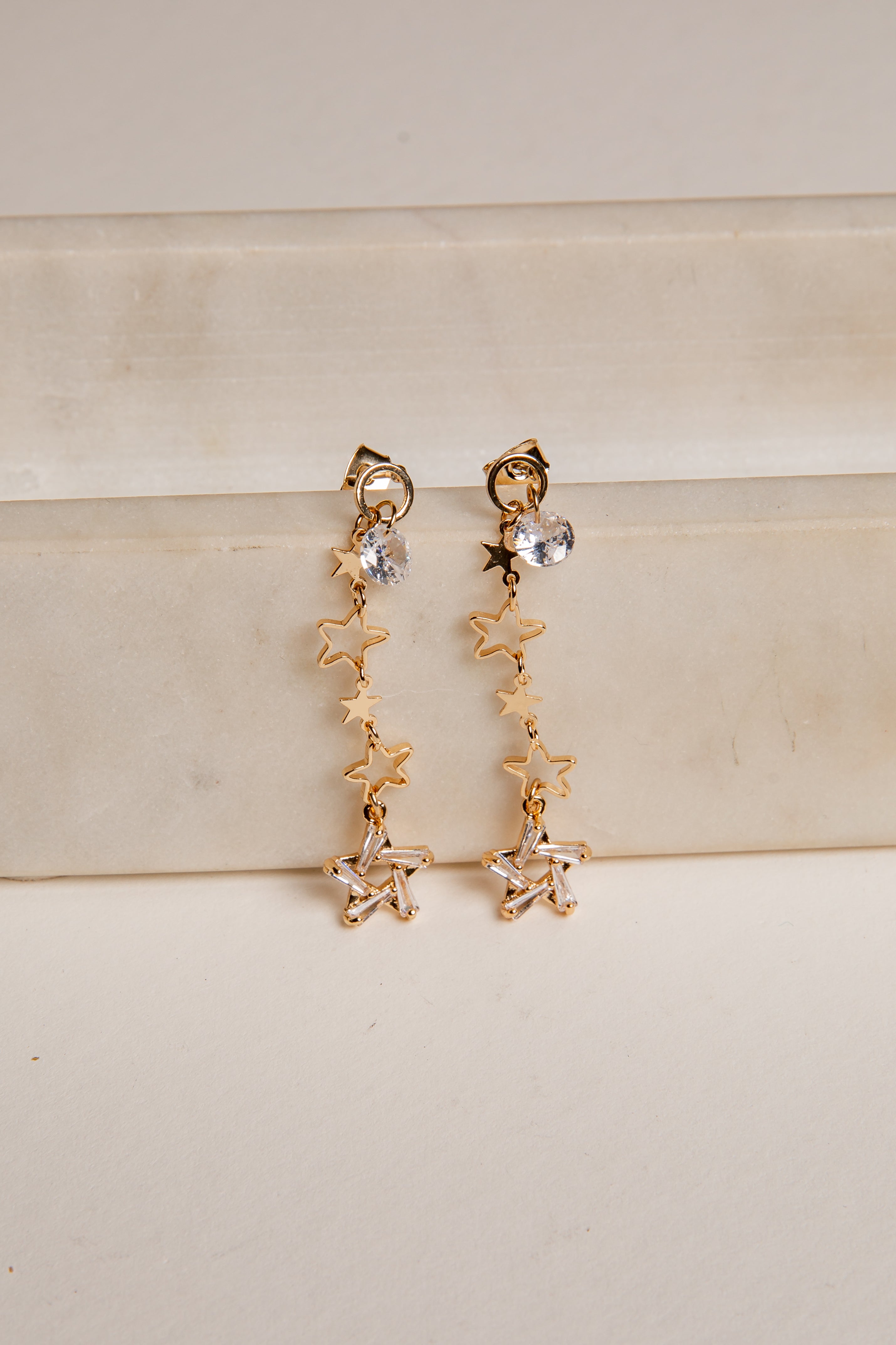 Gold star-shaped earrings on a beige surface
