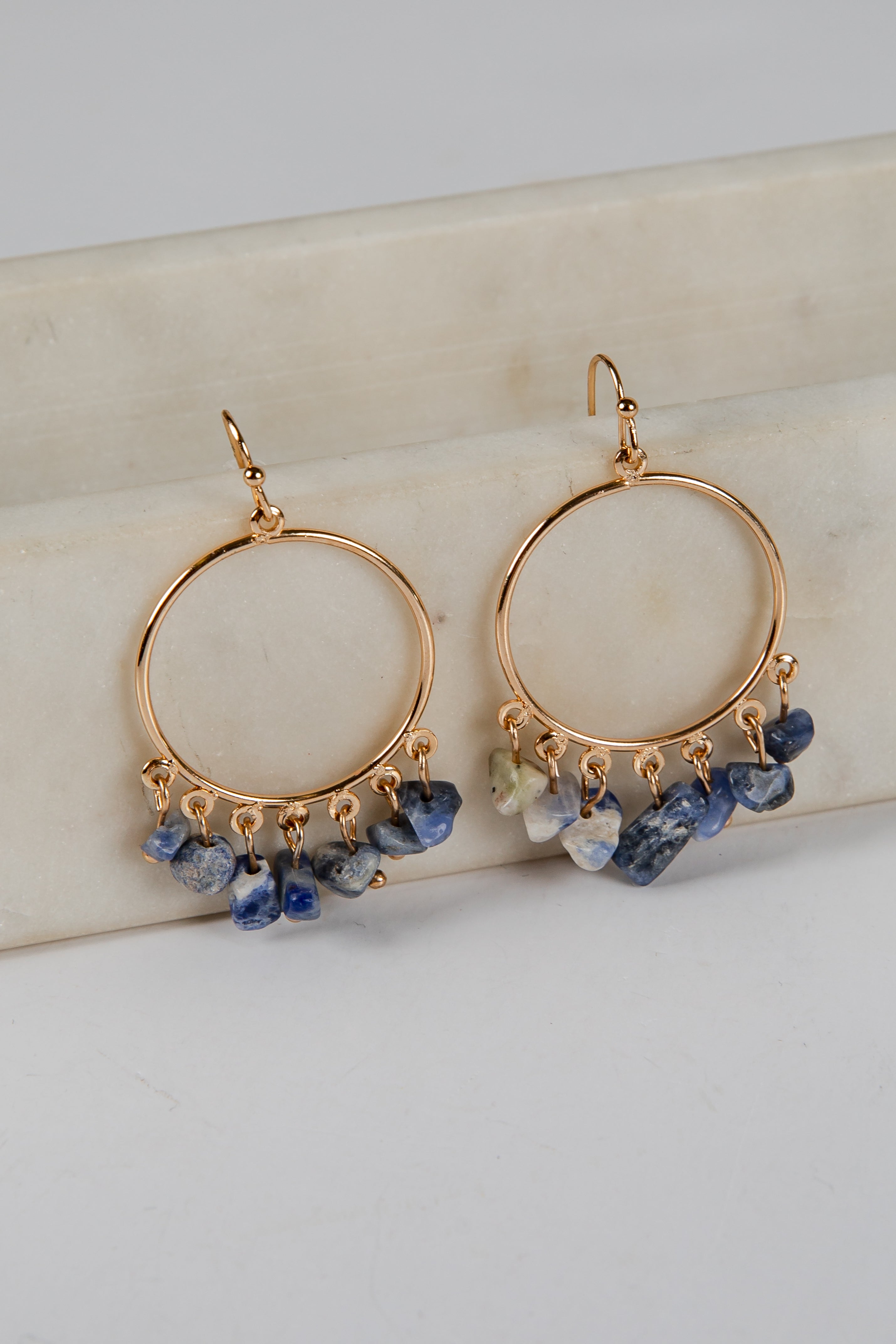 Gold hoop earrings with blue stone drops on a light background
