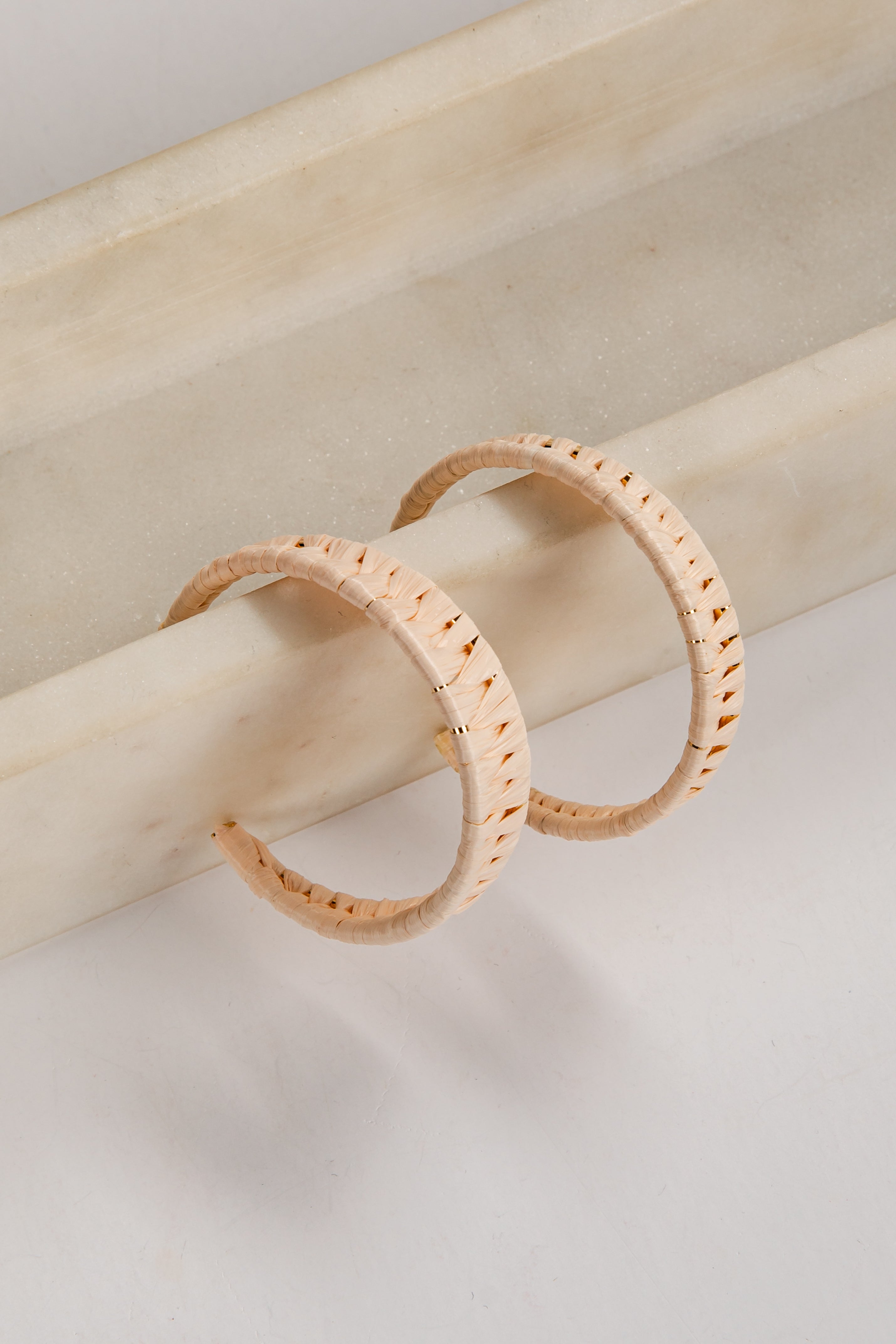 Two gold hoop earrings on a light wooden stick against a neutral background