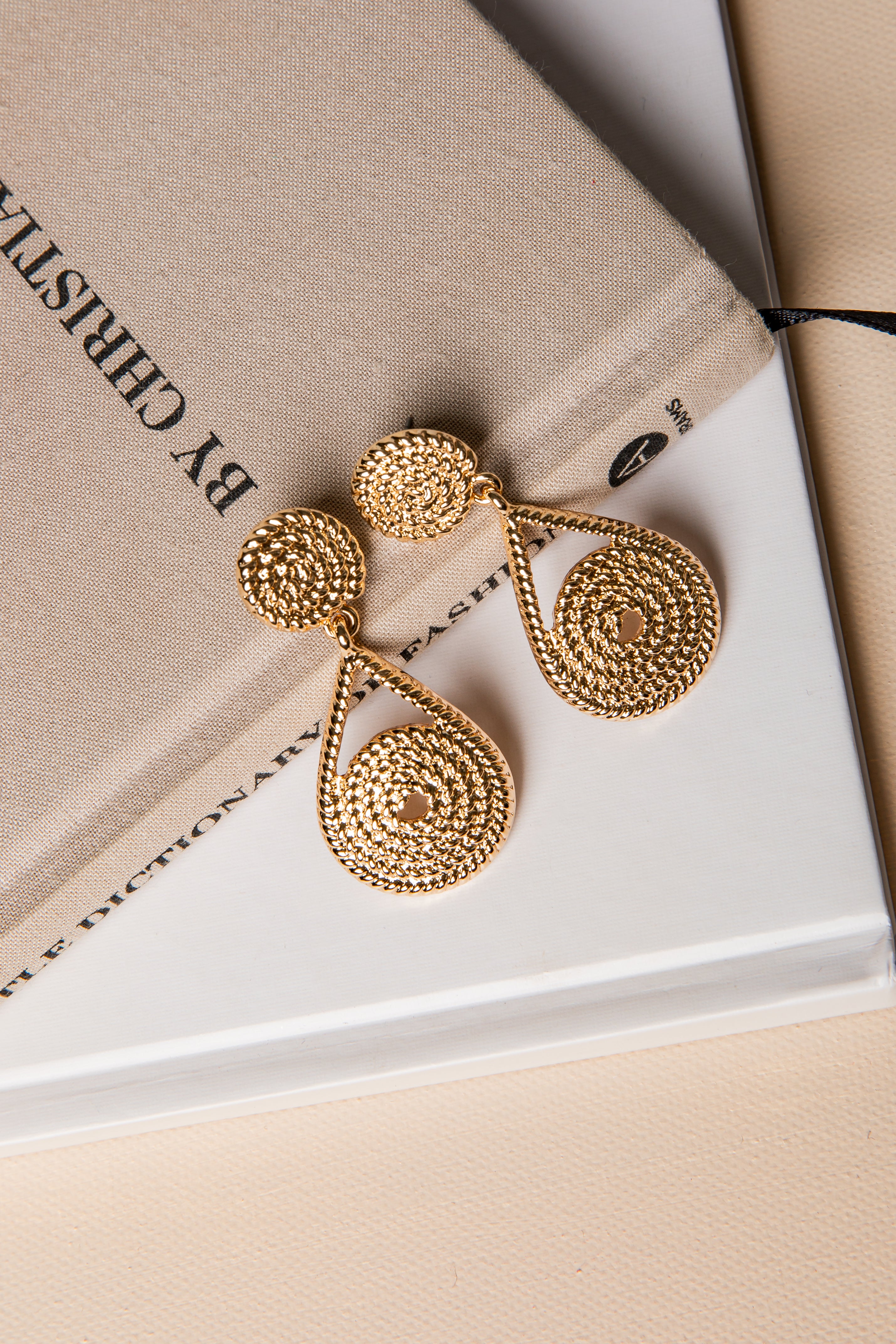 Gold earrings on a beige surface with &