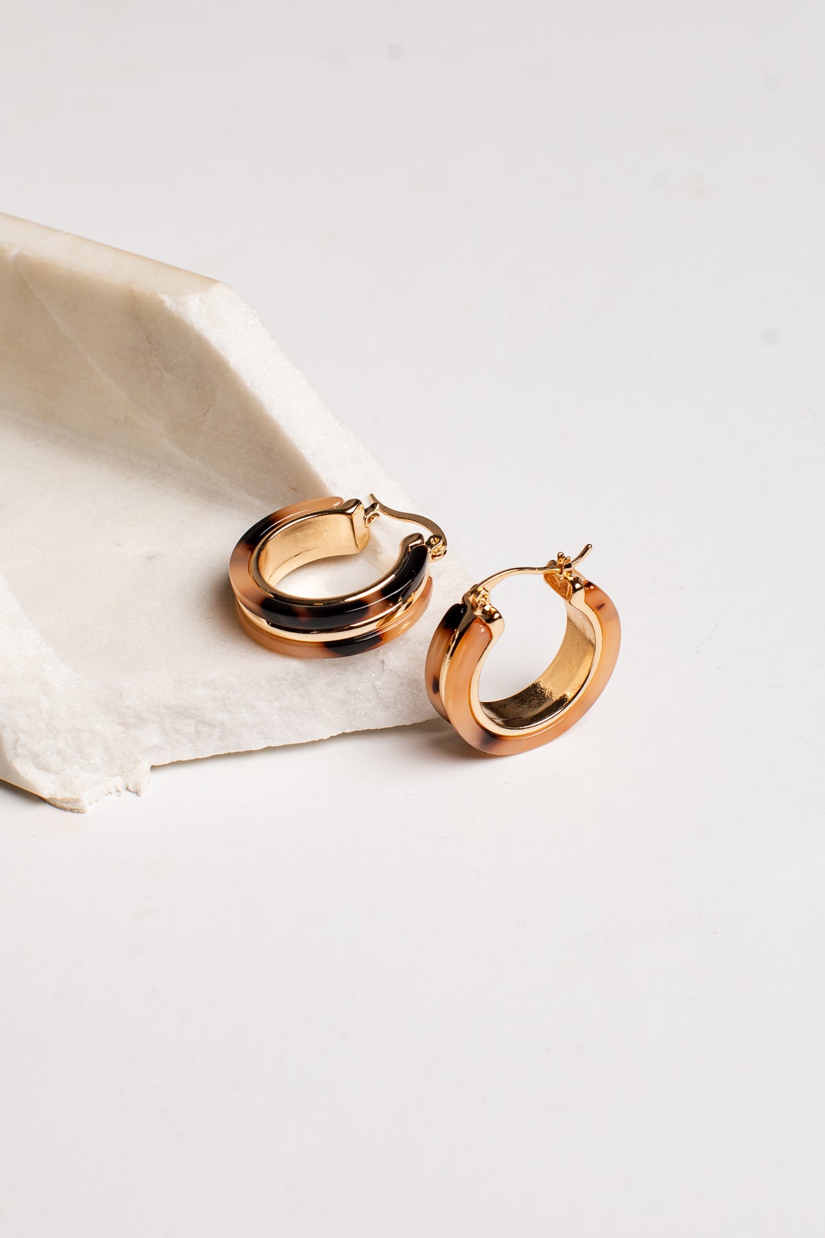 A pair of polished rose gold hoop earrings resting on a textured white paper napkin against a clean white background.