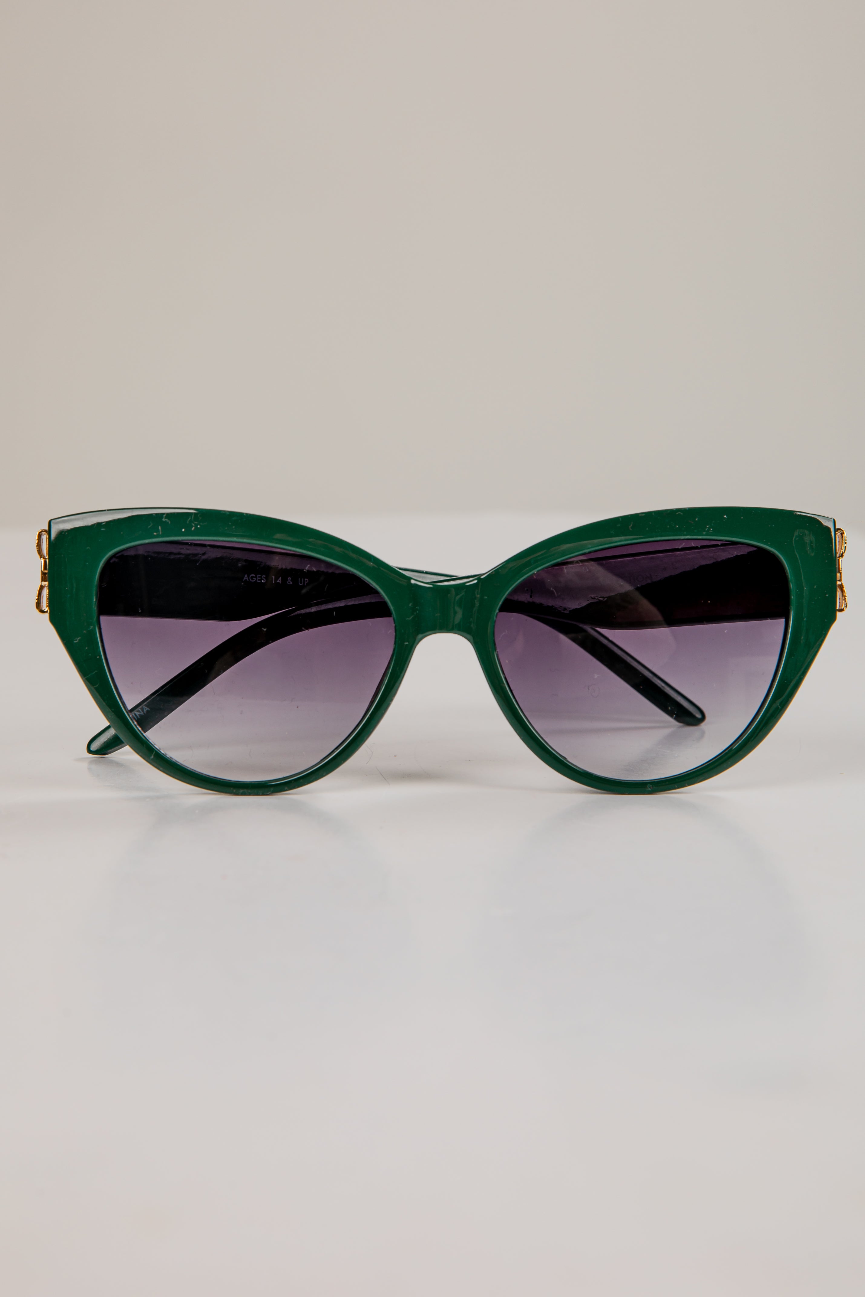 Green cat-eye sunglasses with gold accents on a light gray background