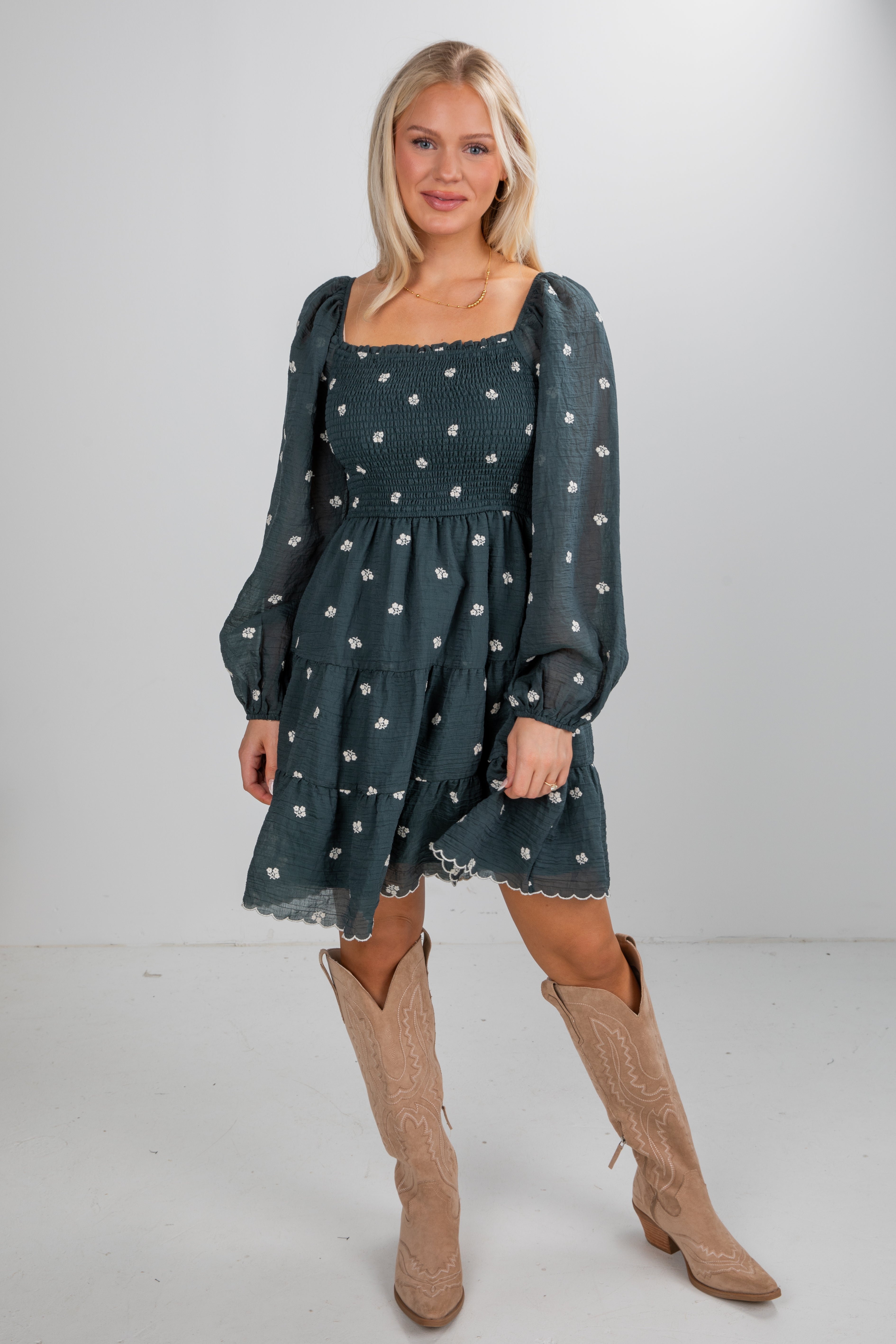 Woman wearing a dark green dress with long sleeves and beige knee-high boots on a white background