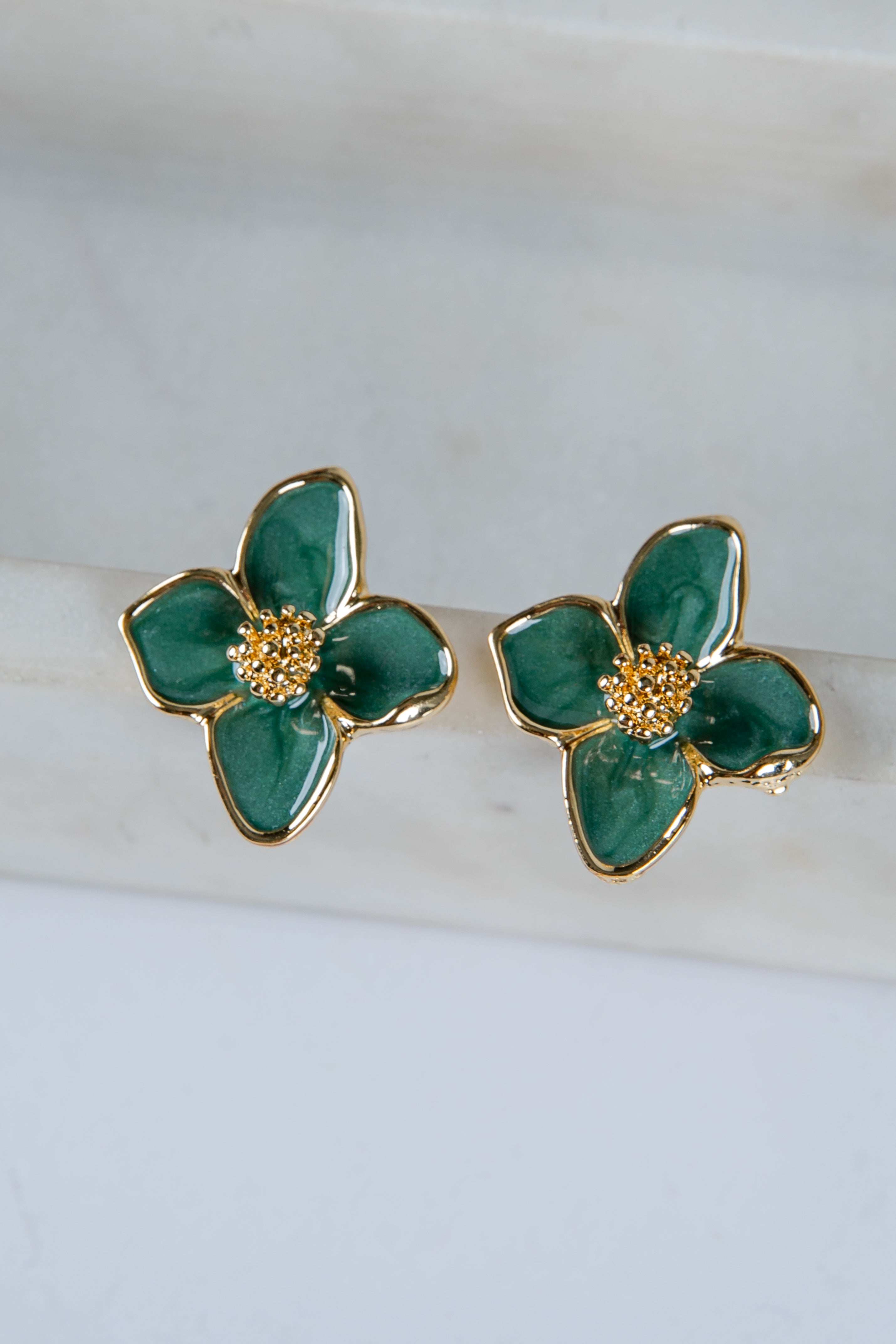 Green floral earrings with gold accents on a white marble surface