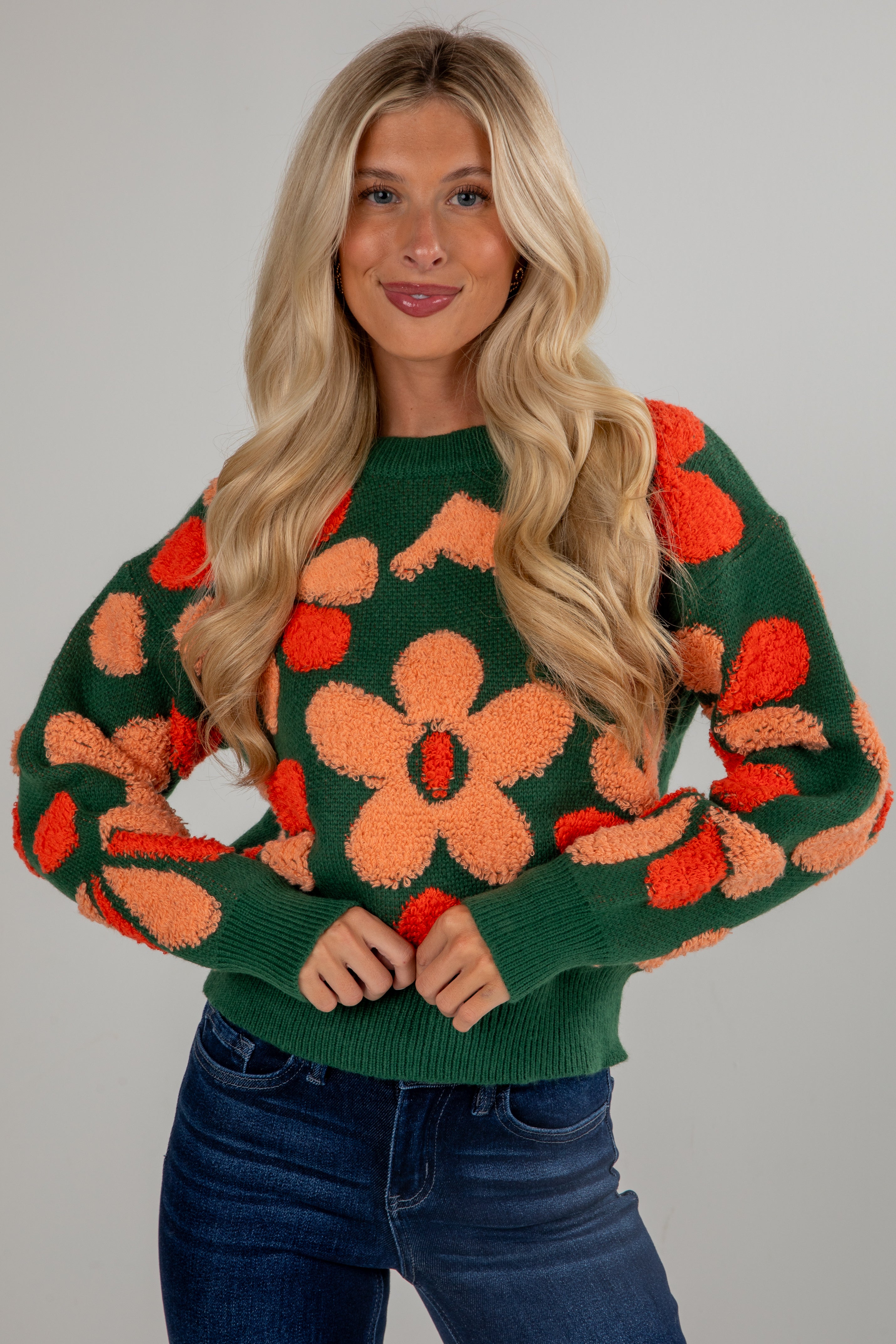 Woman wearing a green sweater with orange floral patterns on a plain background