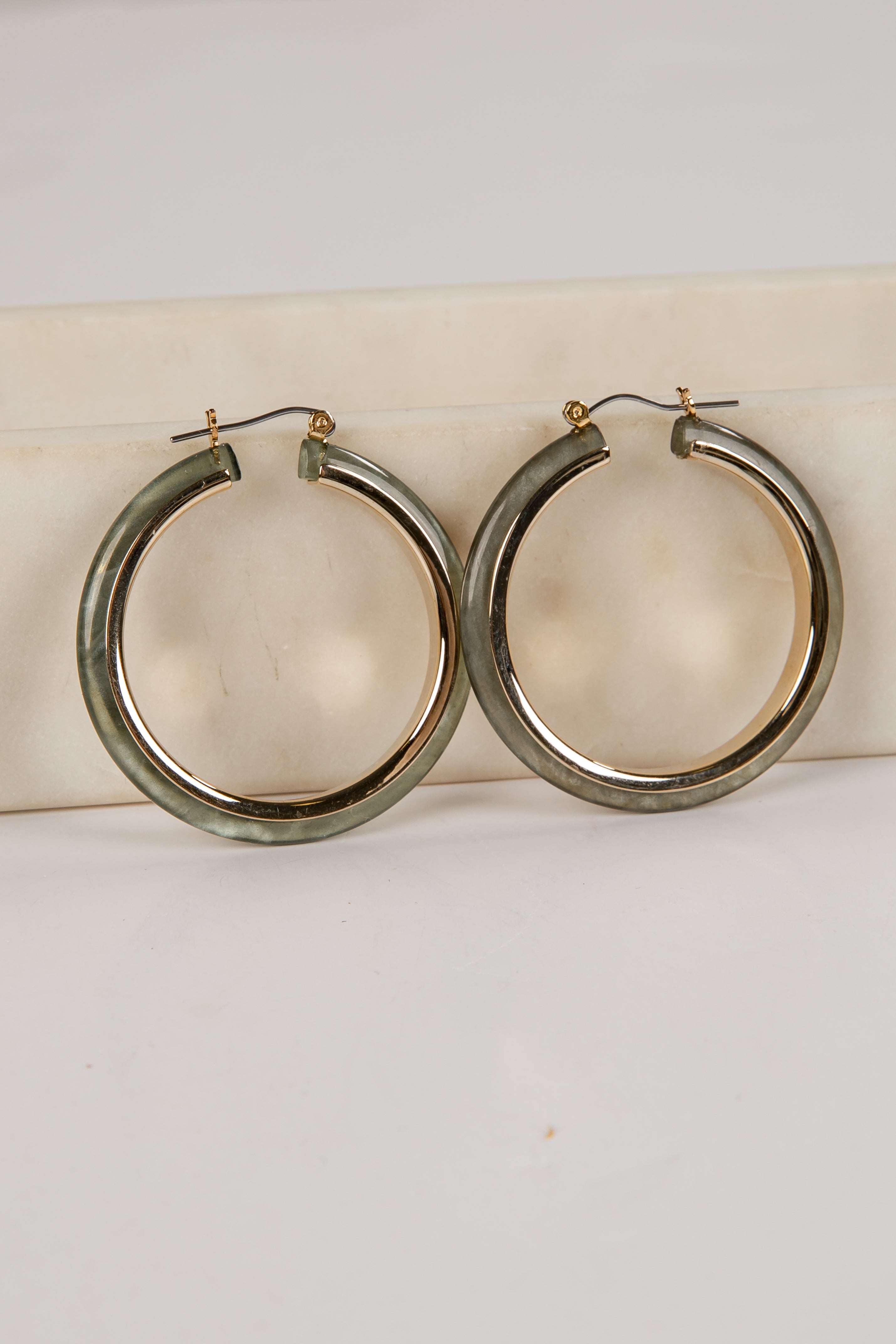 Gold hoop earrings on a white cushion with a light gray background