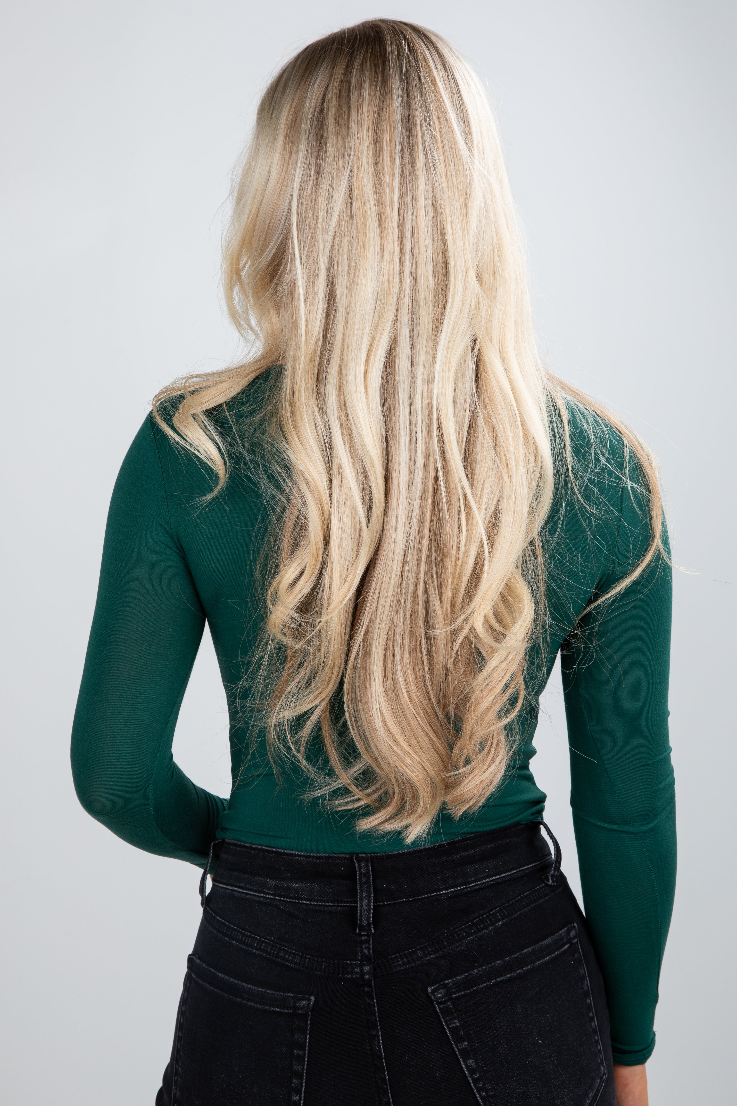 Person wearing a green long-sleeve top with blonde hair flowing over the shoulders on a plain background