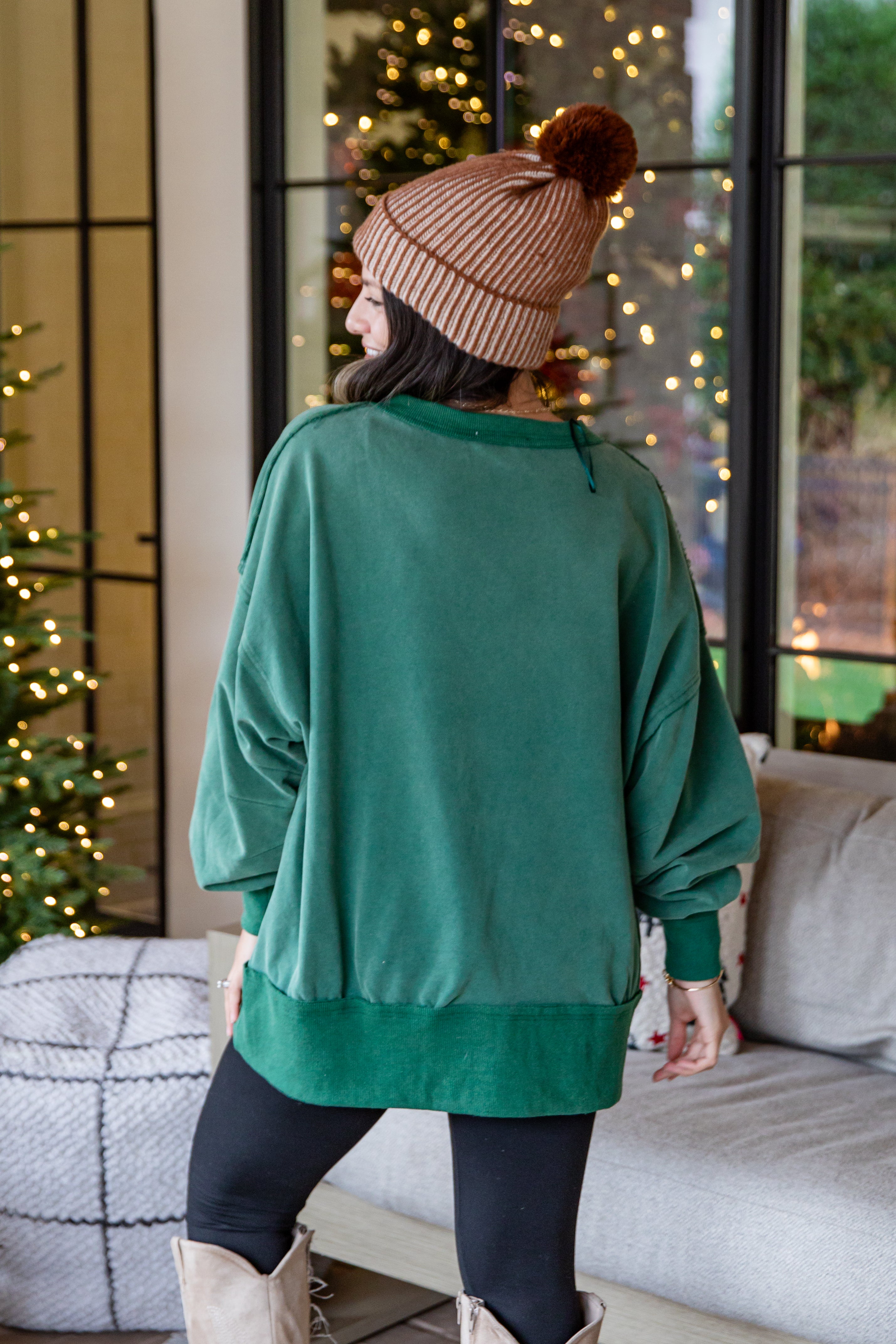 Person wearing a green sweater and brown beanie in a cozy living room with Christmas decorations.