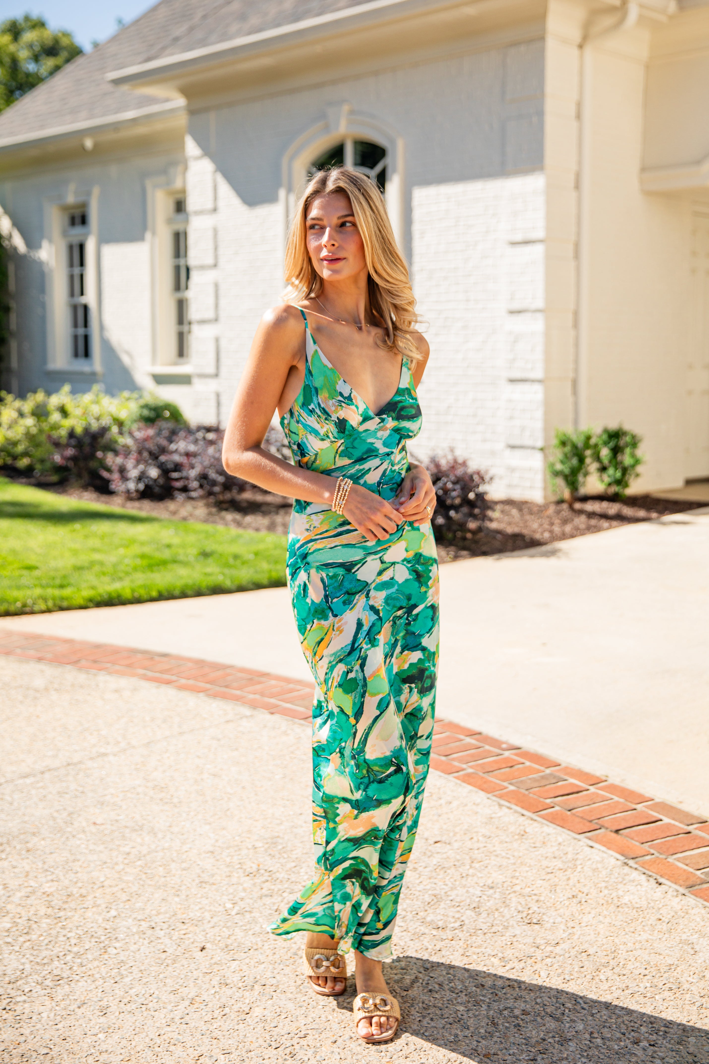 Woman in a green floral dress standing in front of a house.