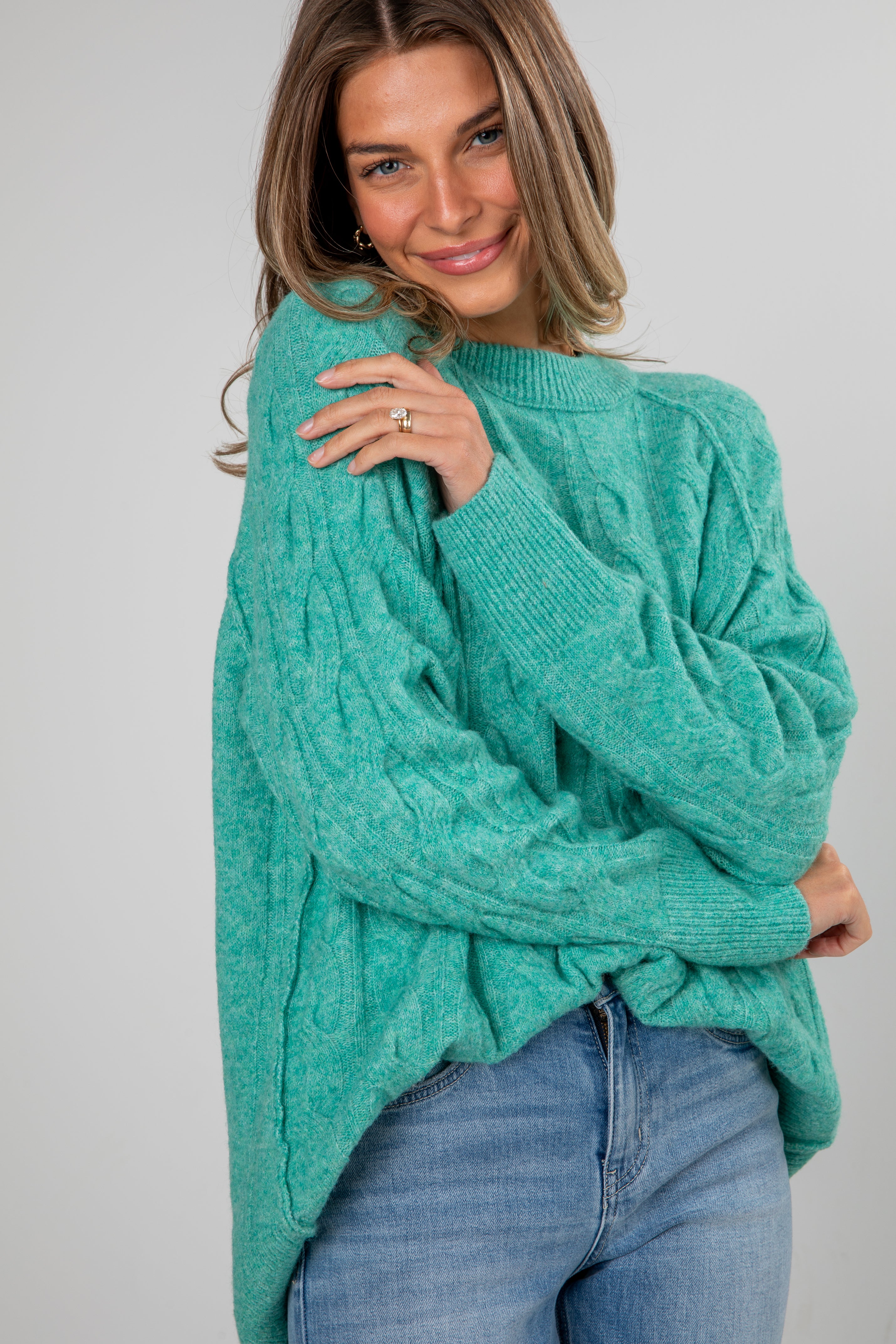 Woman wearing a teal sweater and blue jeans against a plain background