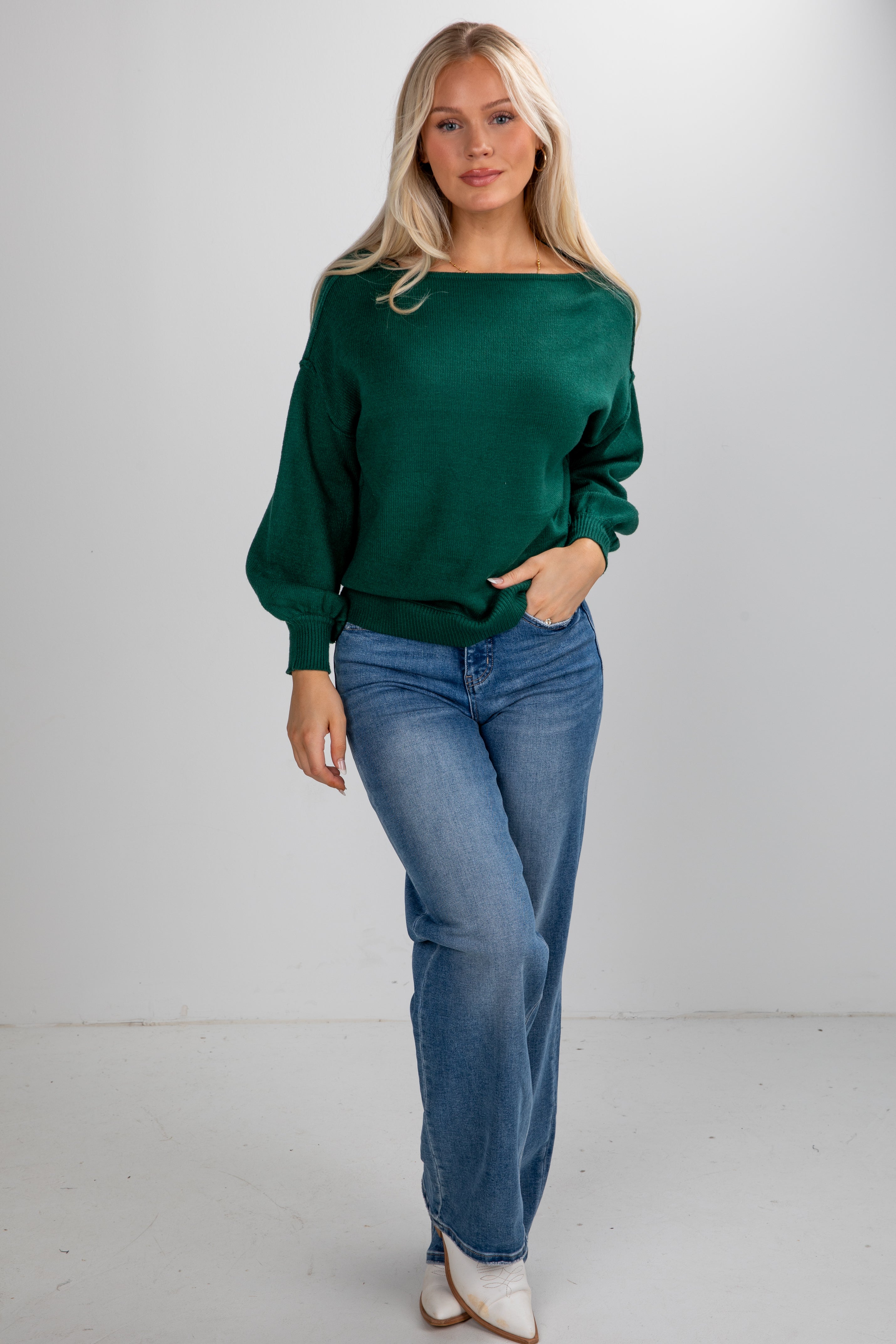 Woman wearing a green sweater and blue jeans on a white background