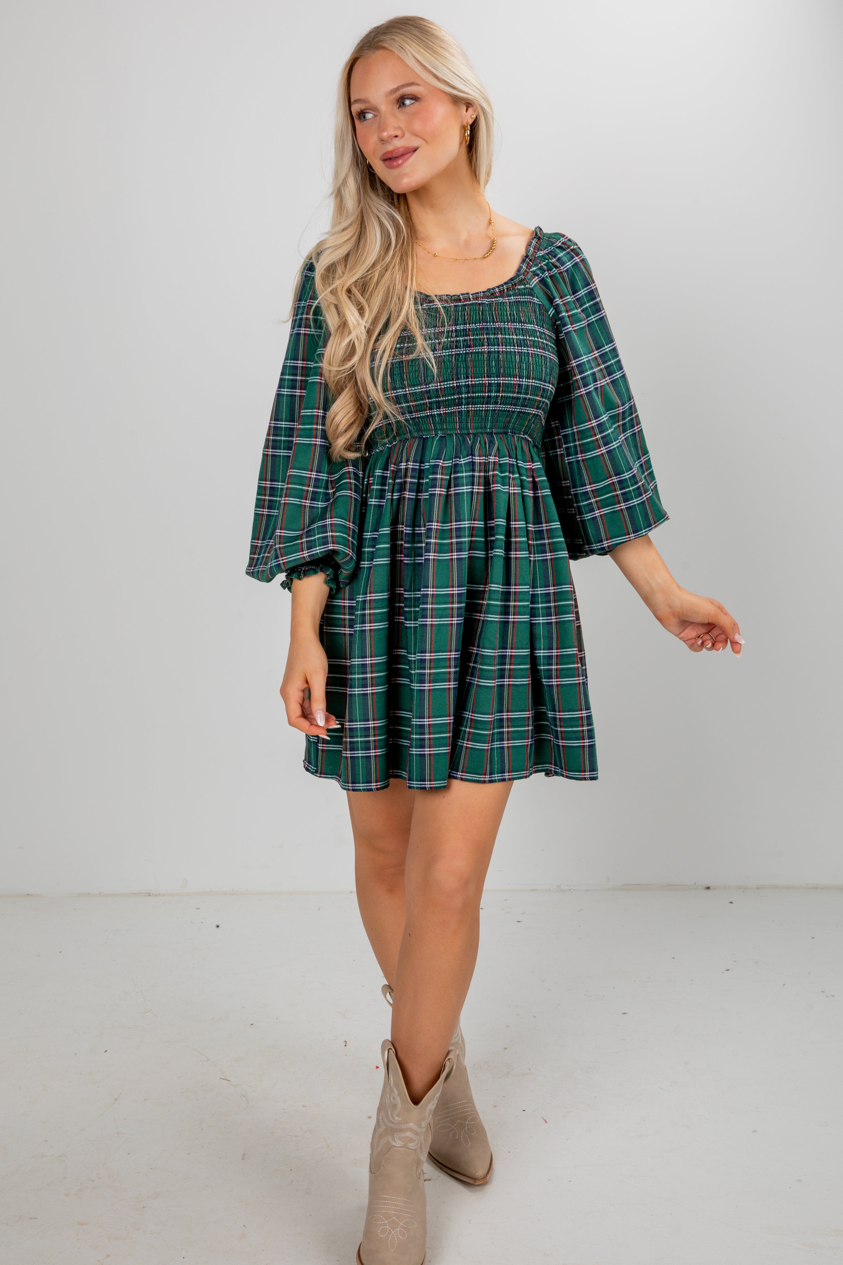 Woman wearing a green plaid dress with beige boots on a white background