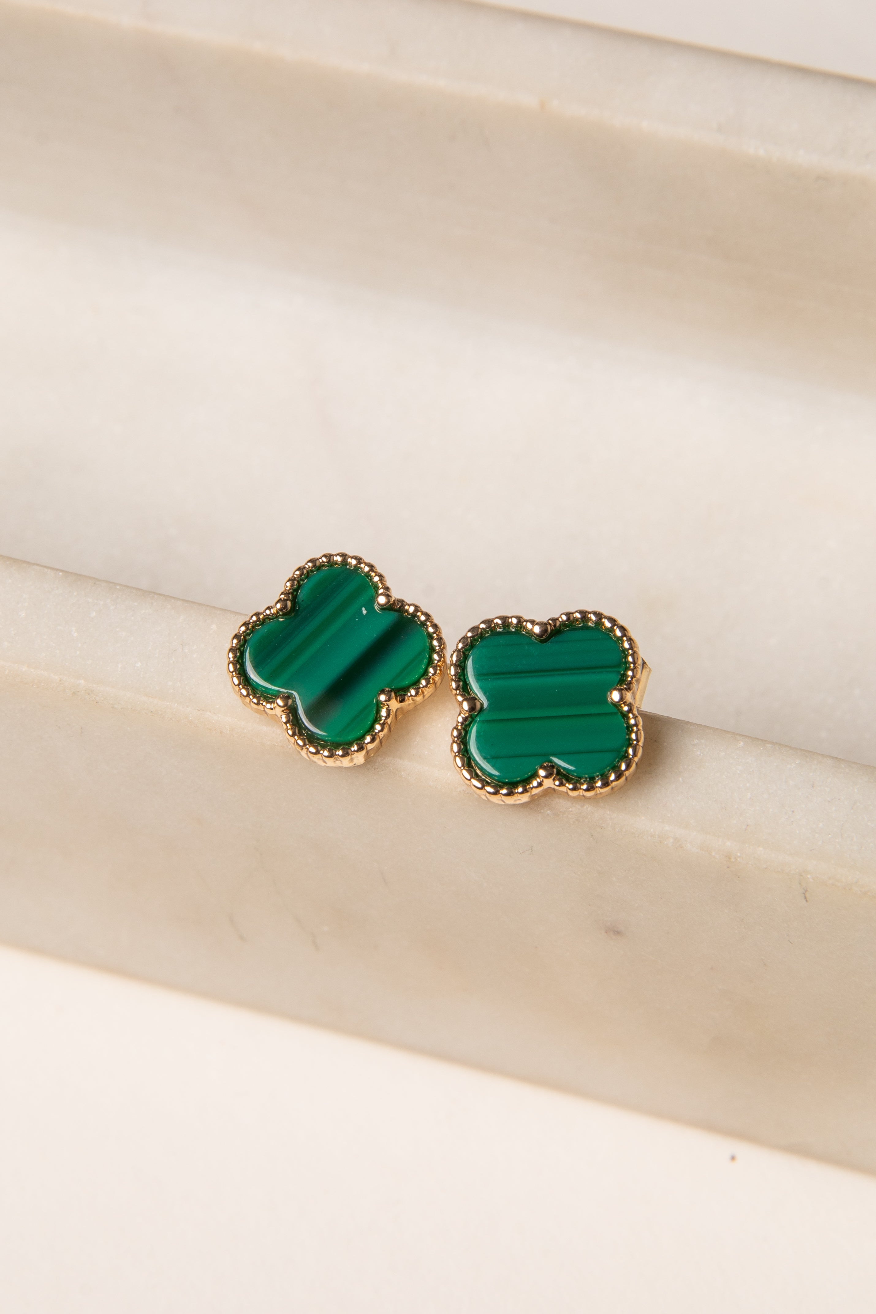 Green clover-shaped earrings on a beige surface
