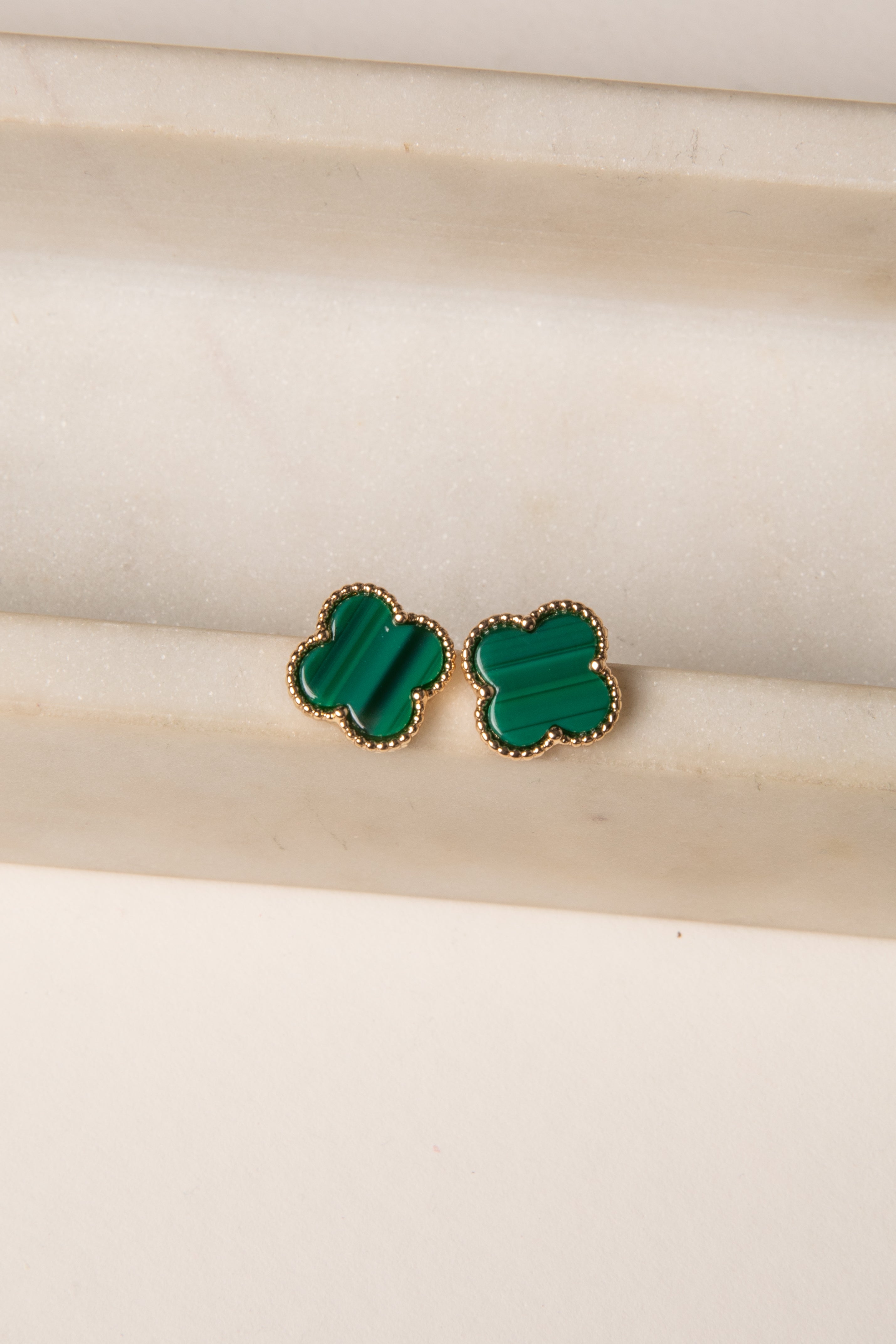 Green clover-shaped earrings on a beige background