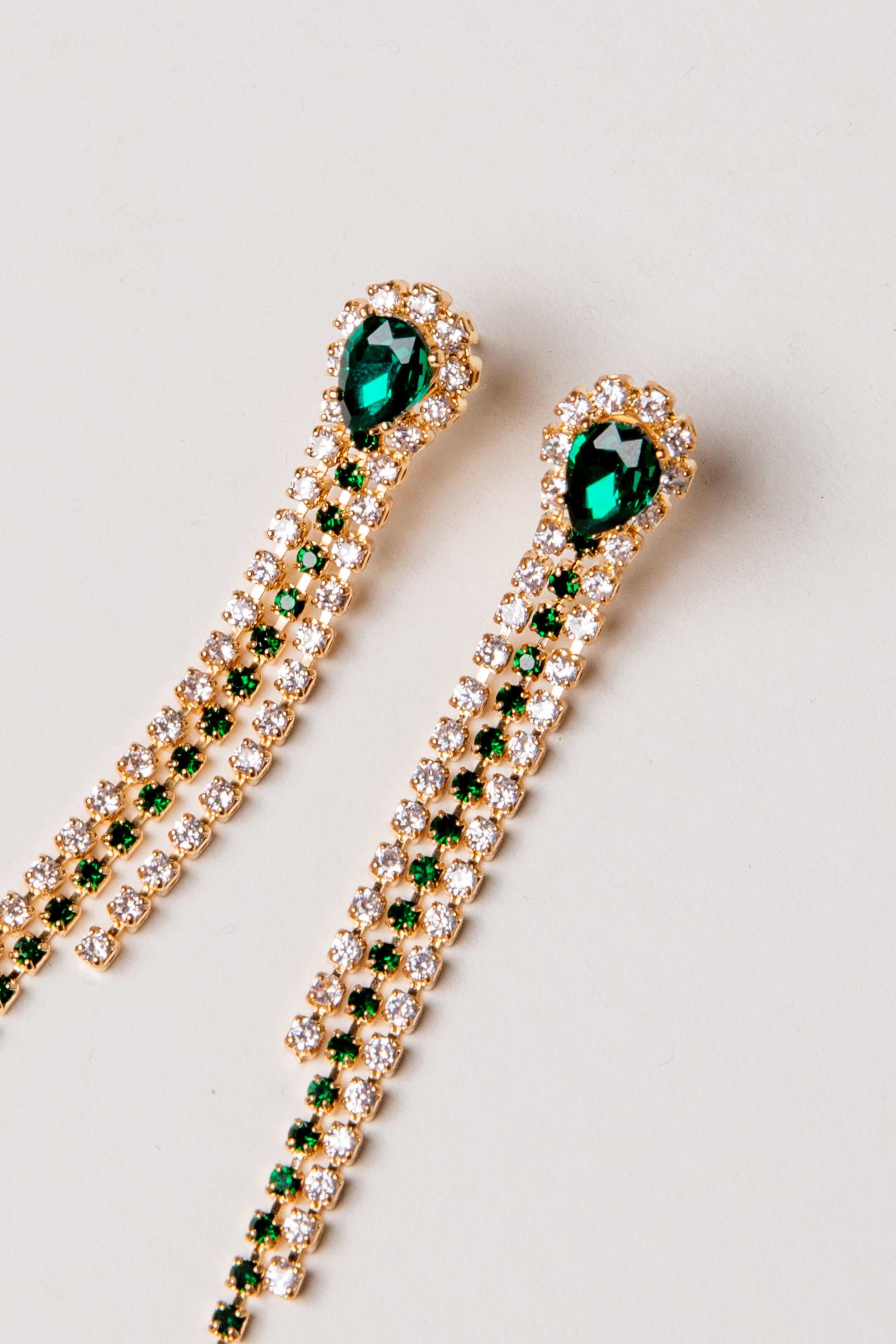 Gold earrings with green gemstones on a light gray background