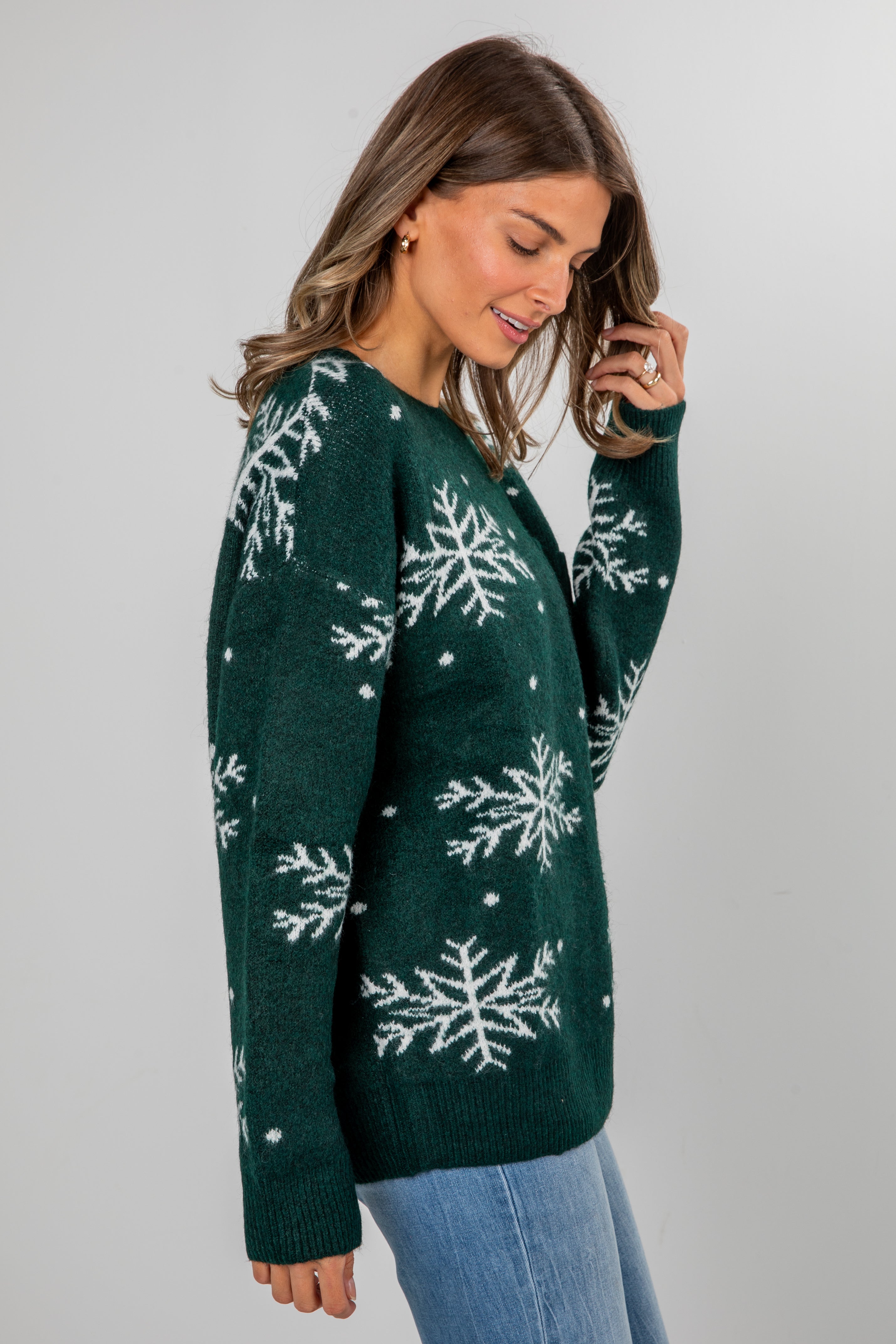 Woman wearing a green sweater with snowflake patterns on a plain background