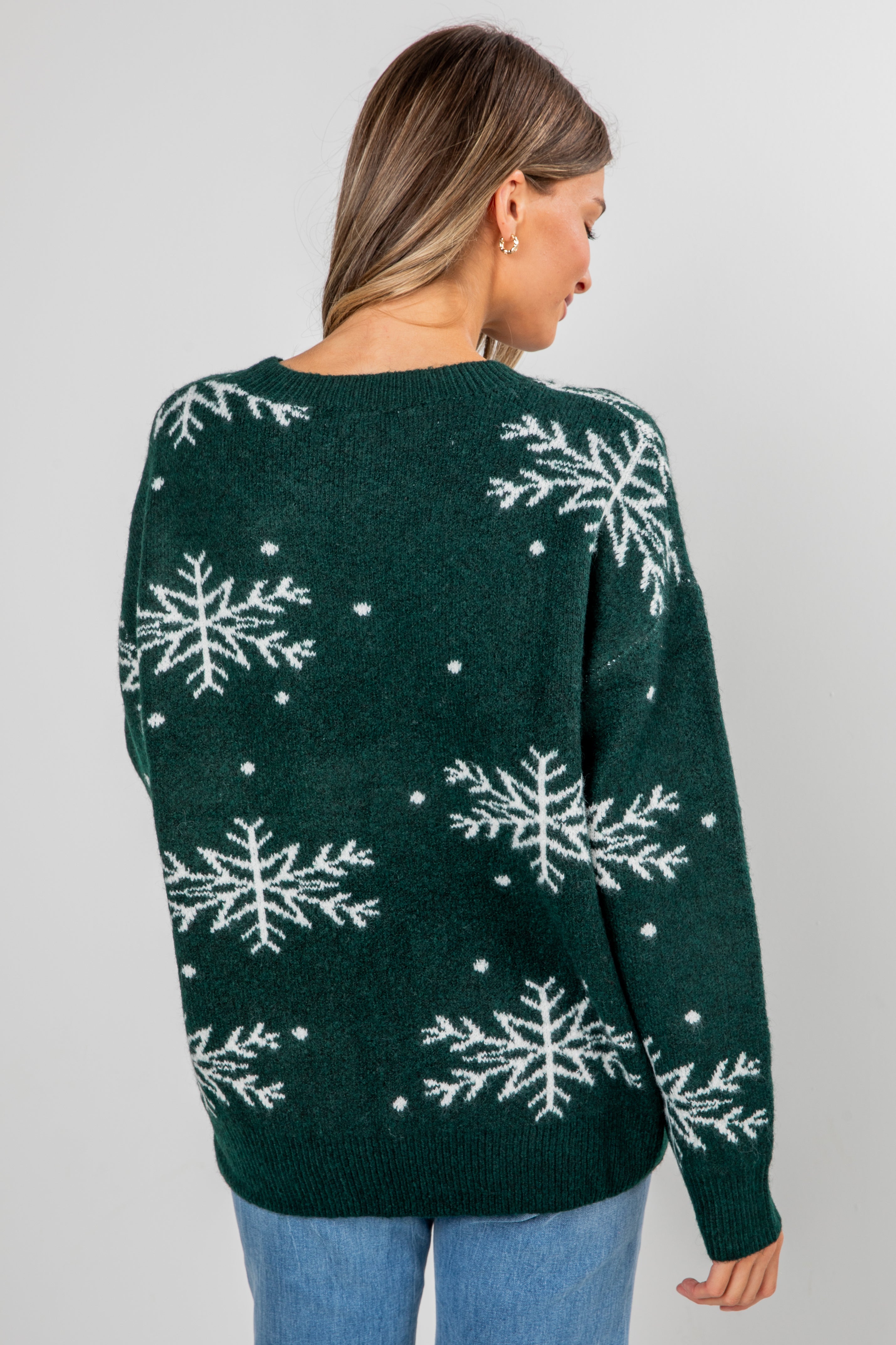 Green sweater with snowflake pattern worn by a person on a gray background