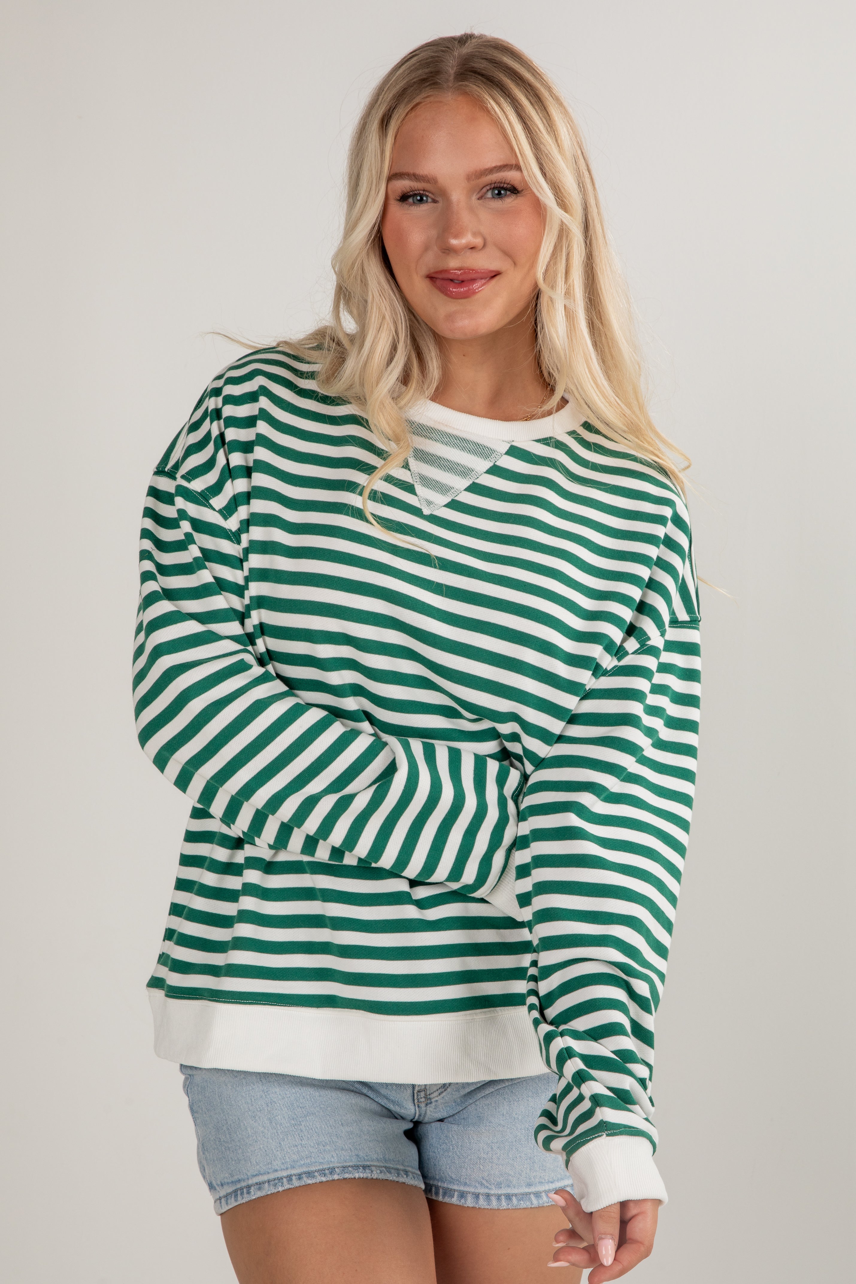 Woman wearing a green and white striped sweater with denim shorts on a plain background