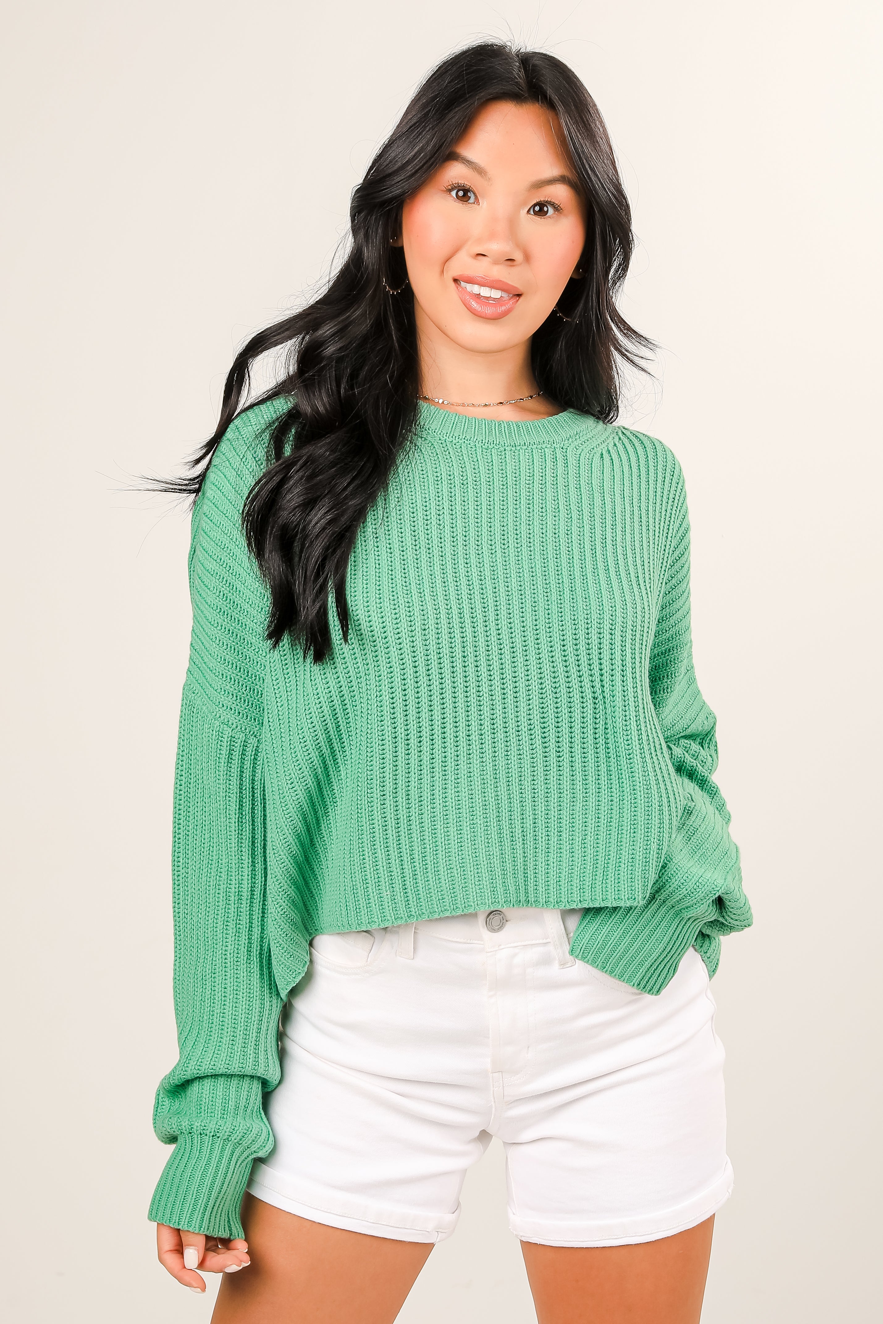 Woman wearing a green sweater and white shorts on a beige background