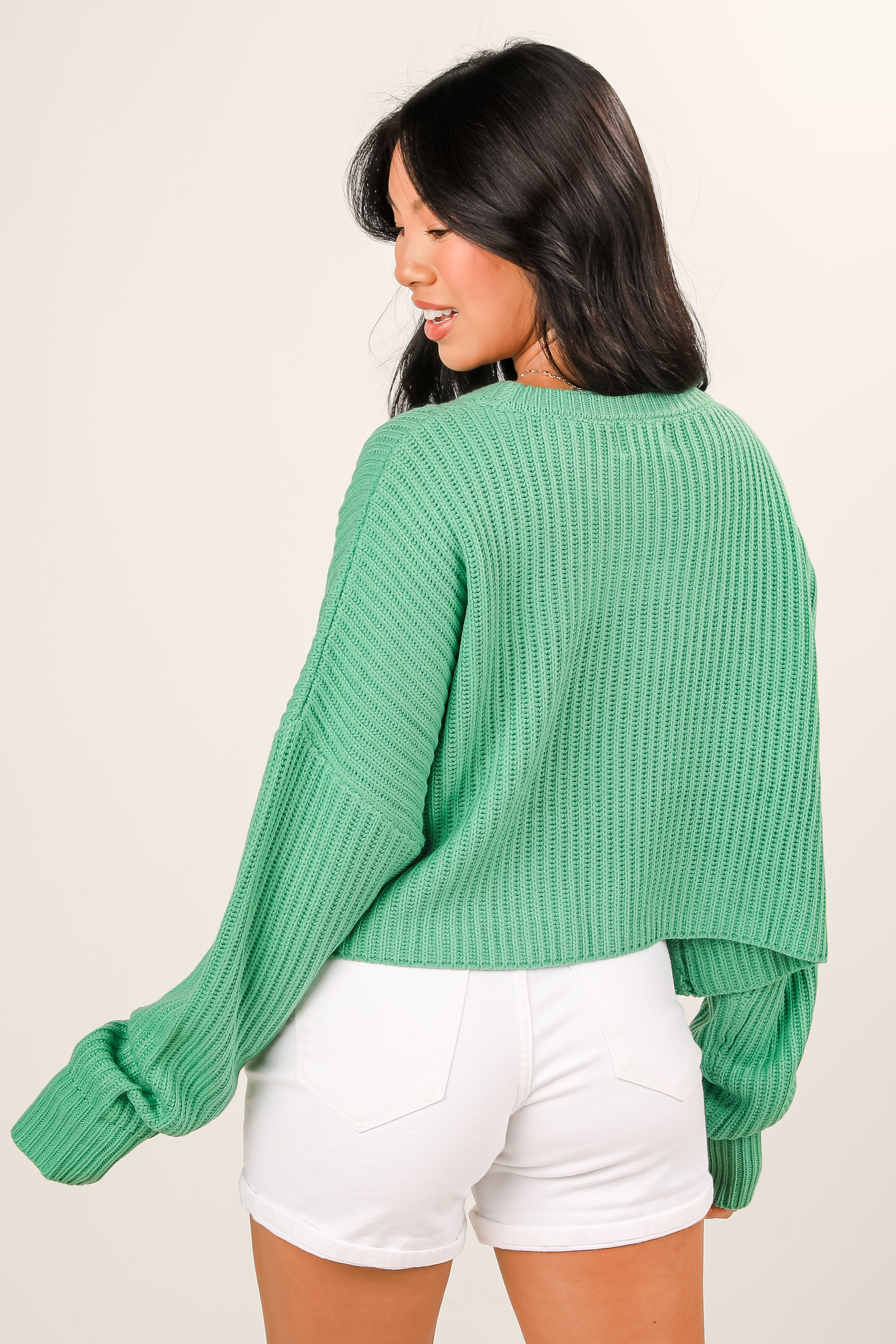 Woman wearing a green sweater and white shorts on a beige background