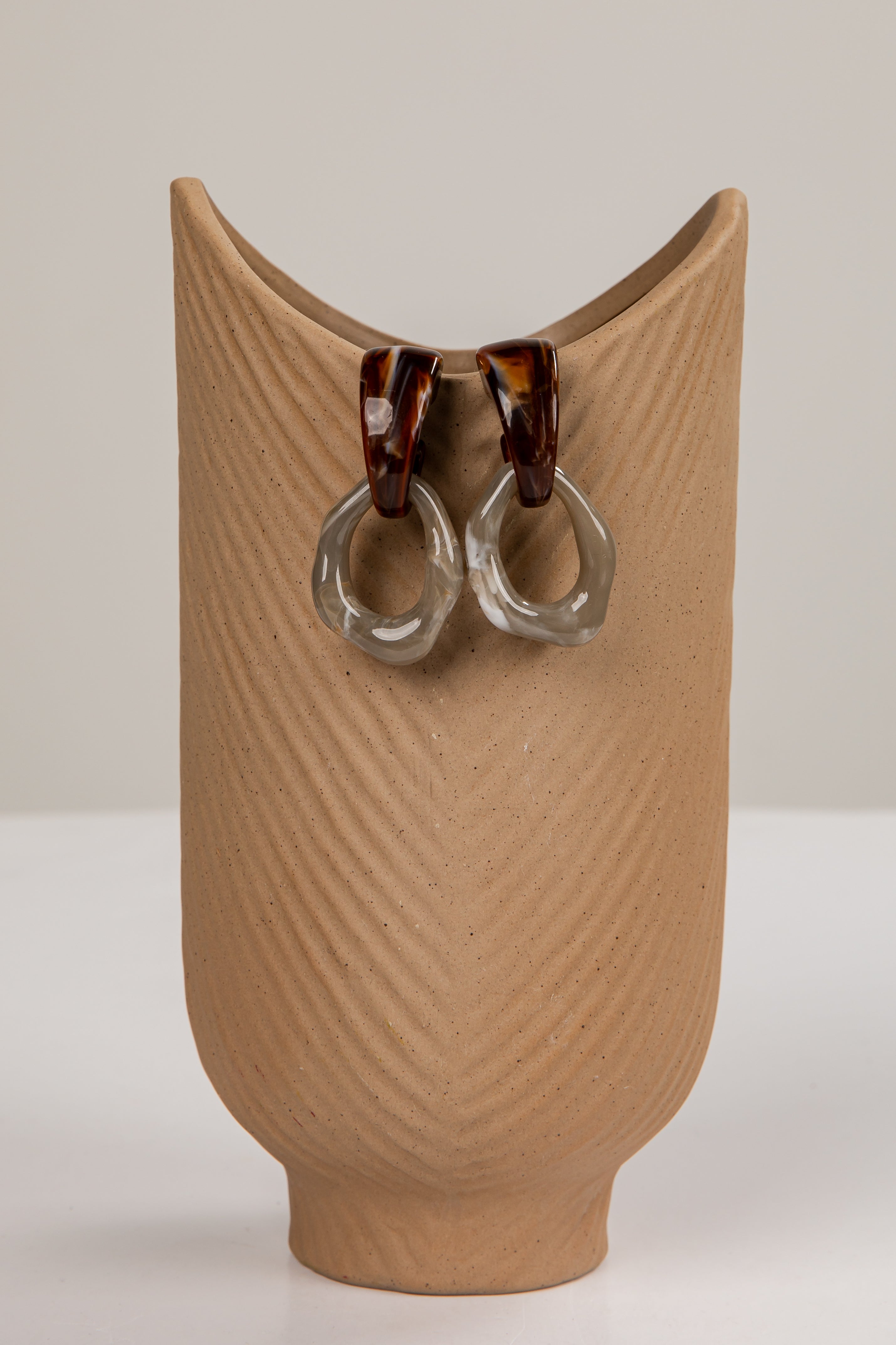 Pair of earrings on a textured brown stand against a plain background