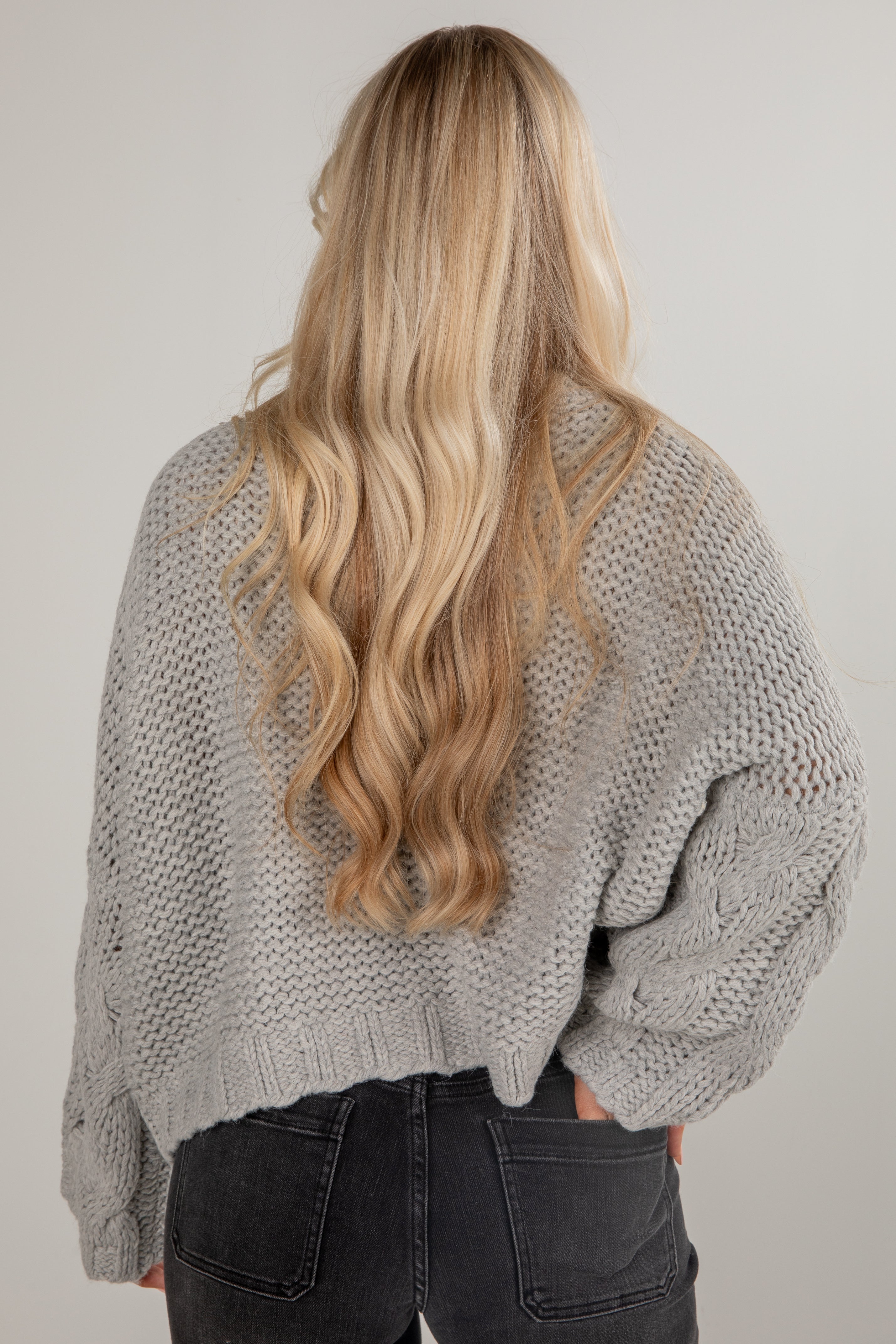 Person wearing a gray knitted sweater and black pants with long blonde hair.