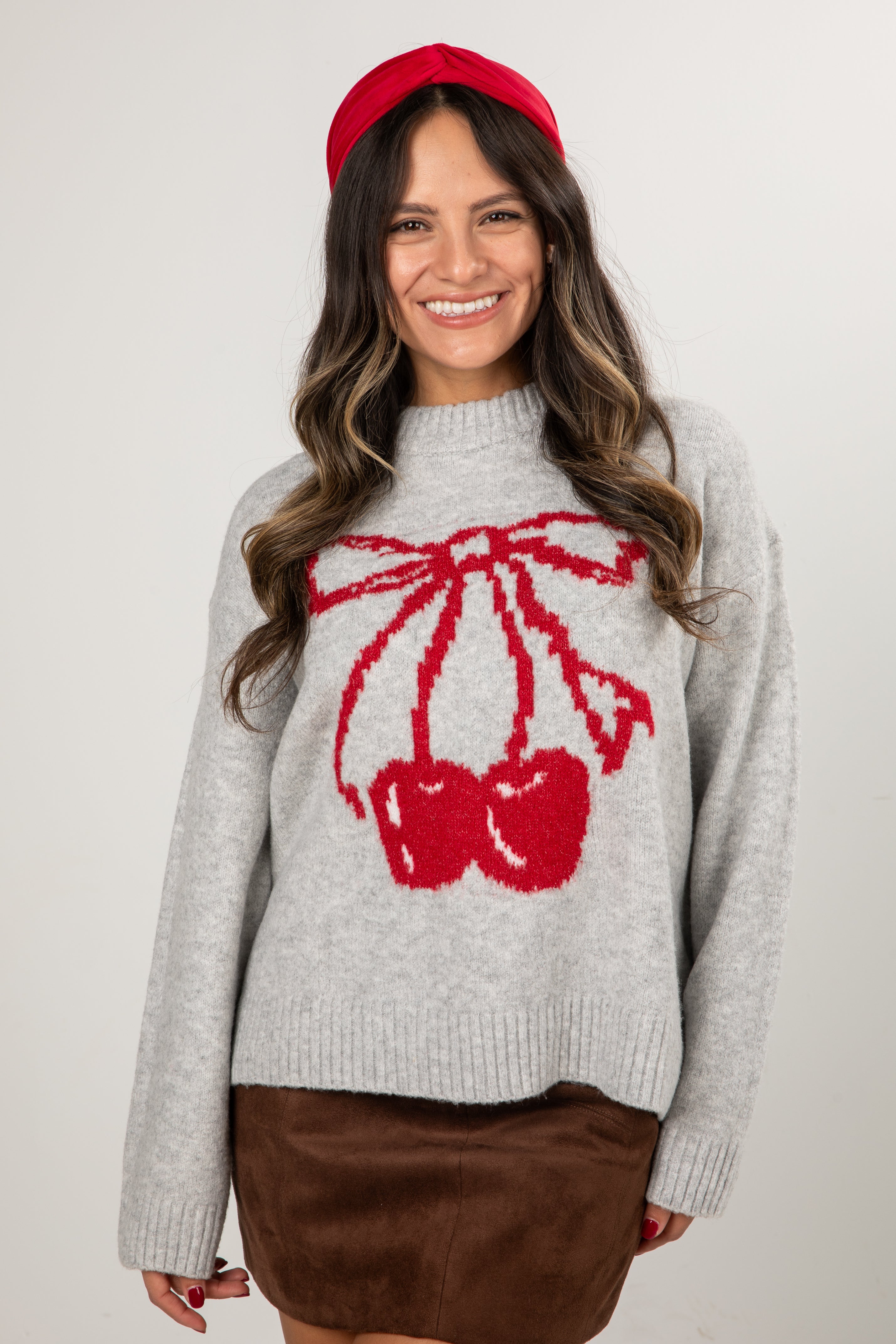 Woman wearing a gray sweater with a red bow design and a red headband against a white background