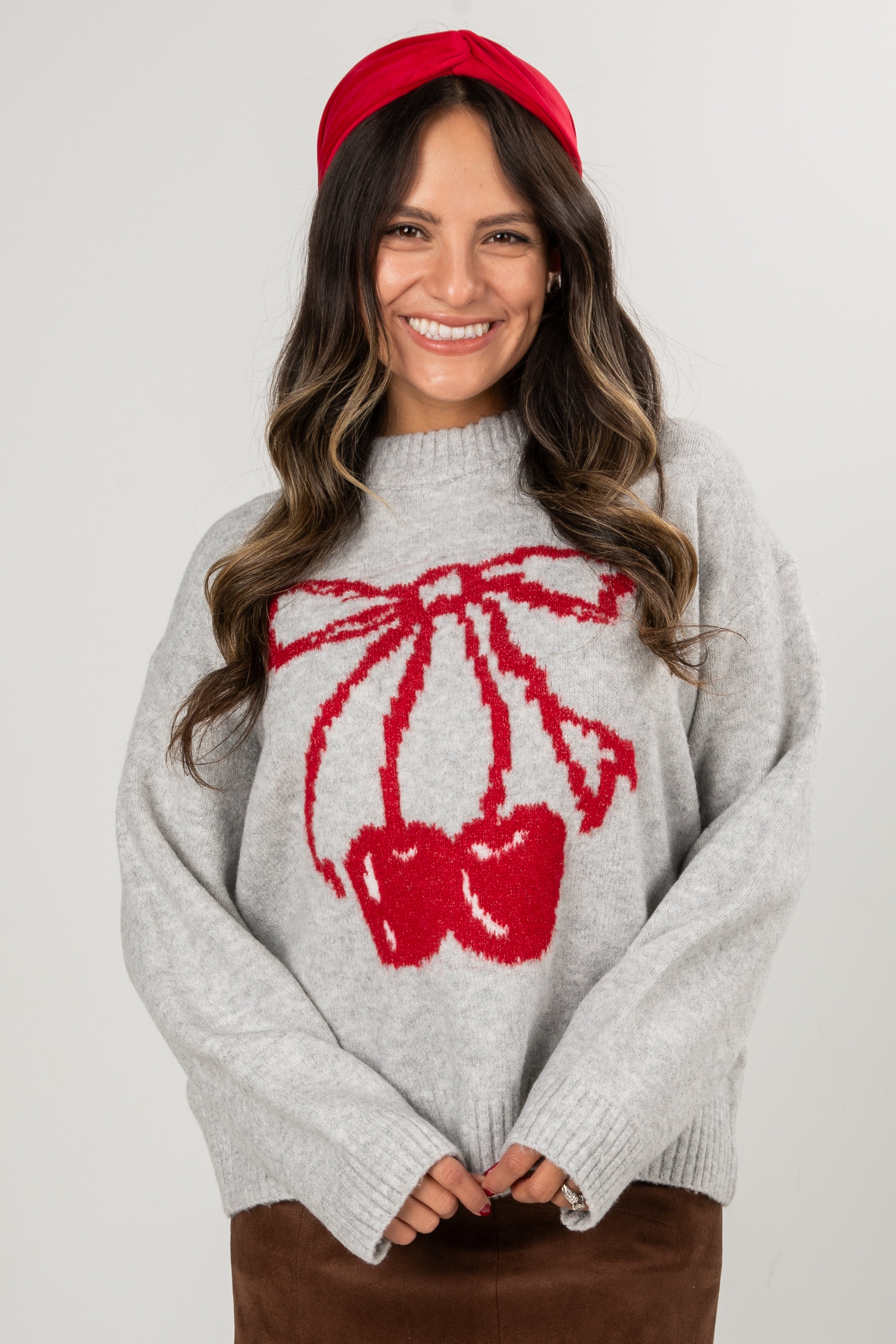 Woman wearing a gray sweater with a red bow design and a red headband against a white background