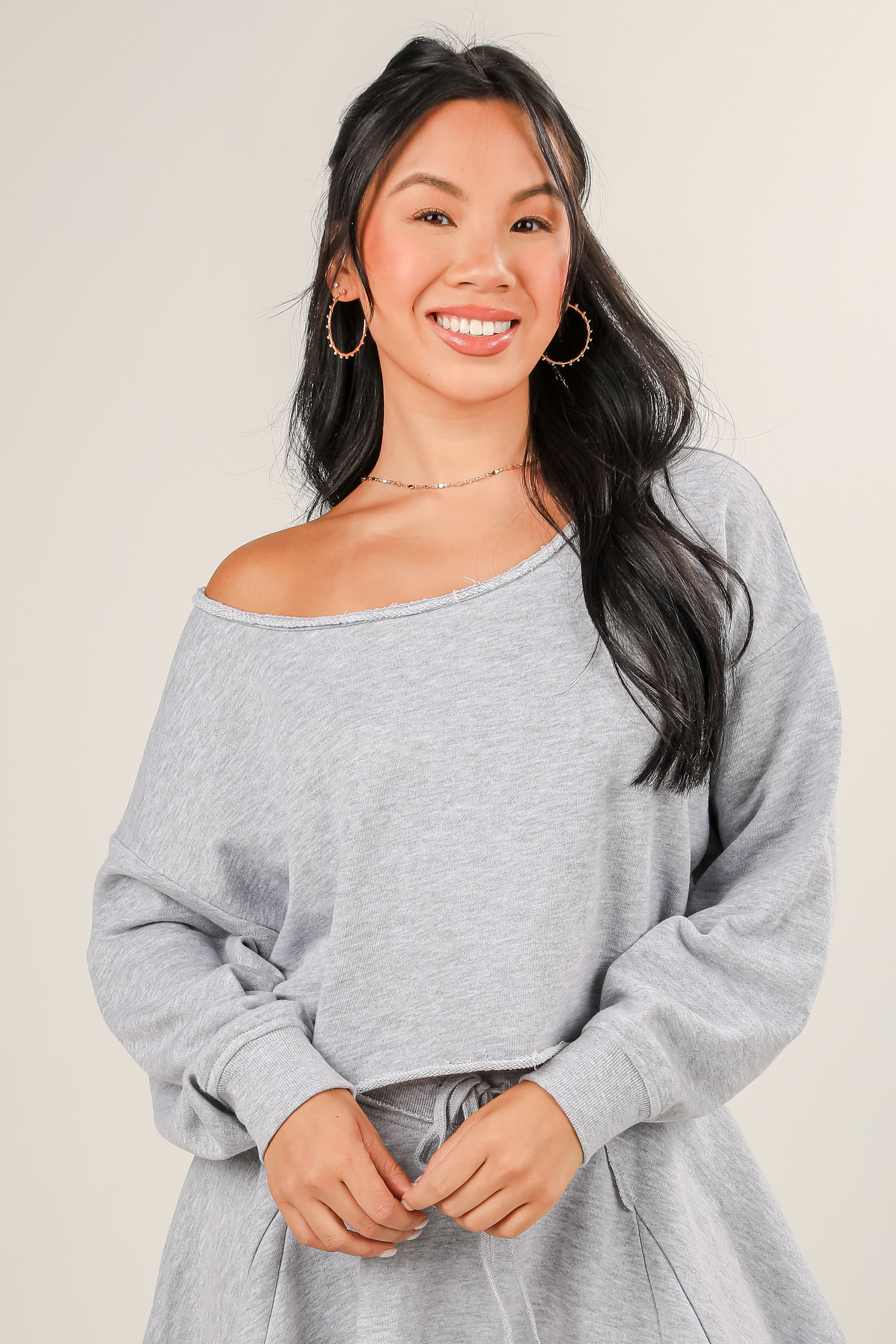 Woman wearing a gray off-shoulder sweater against a plain background