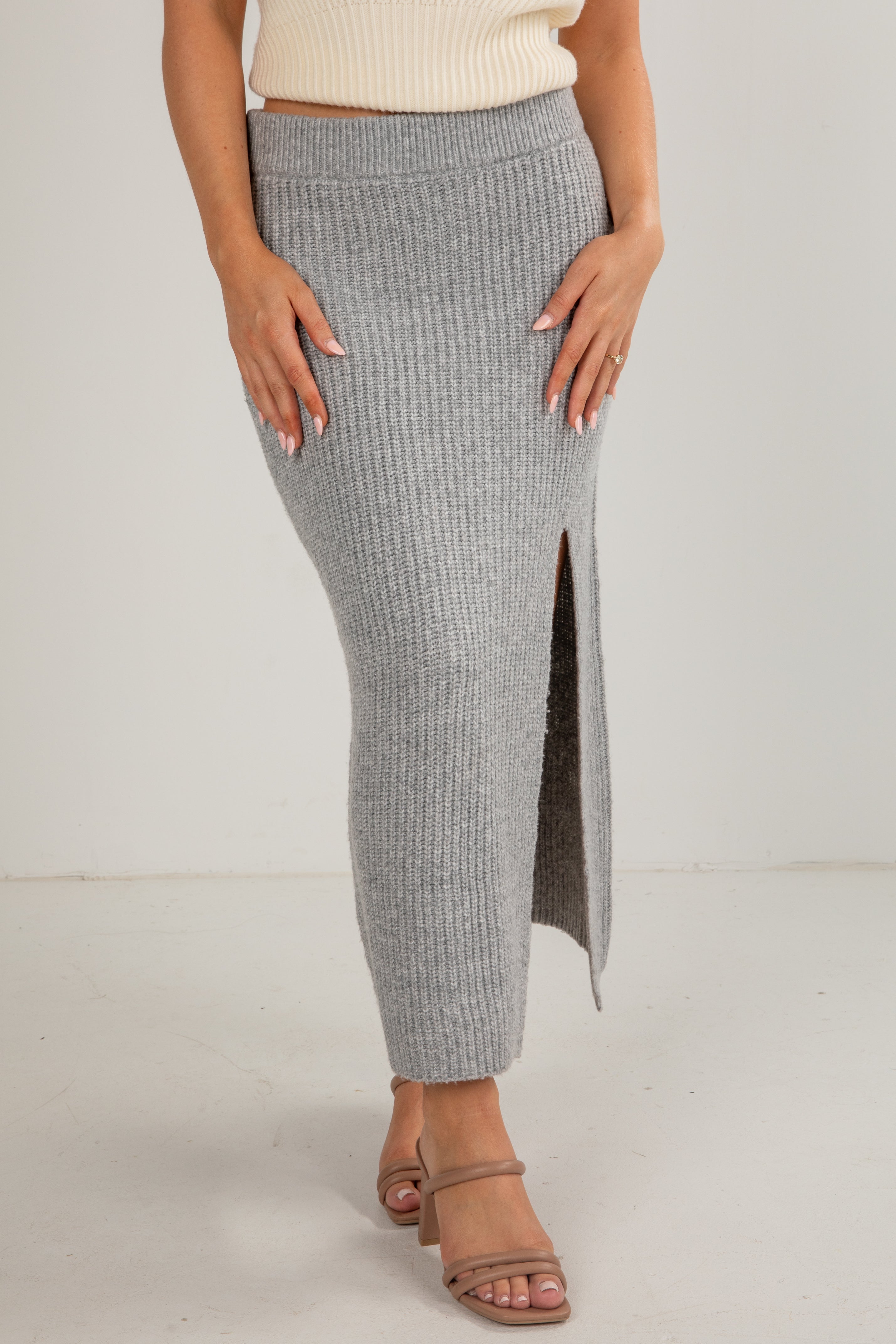 Person wearing a gray ribbed skirt with a white top on a plain background