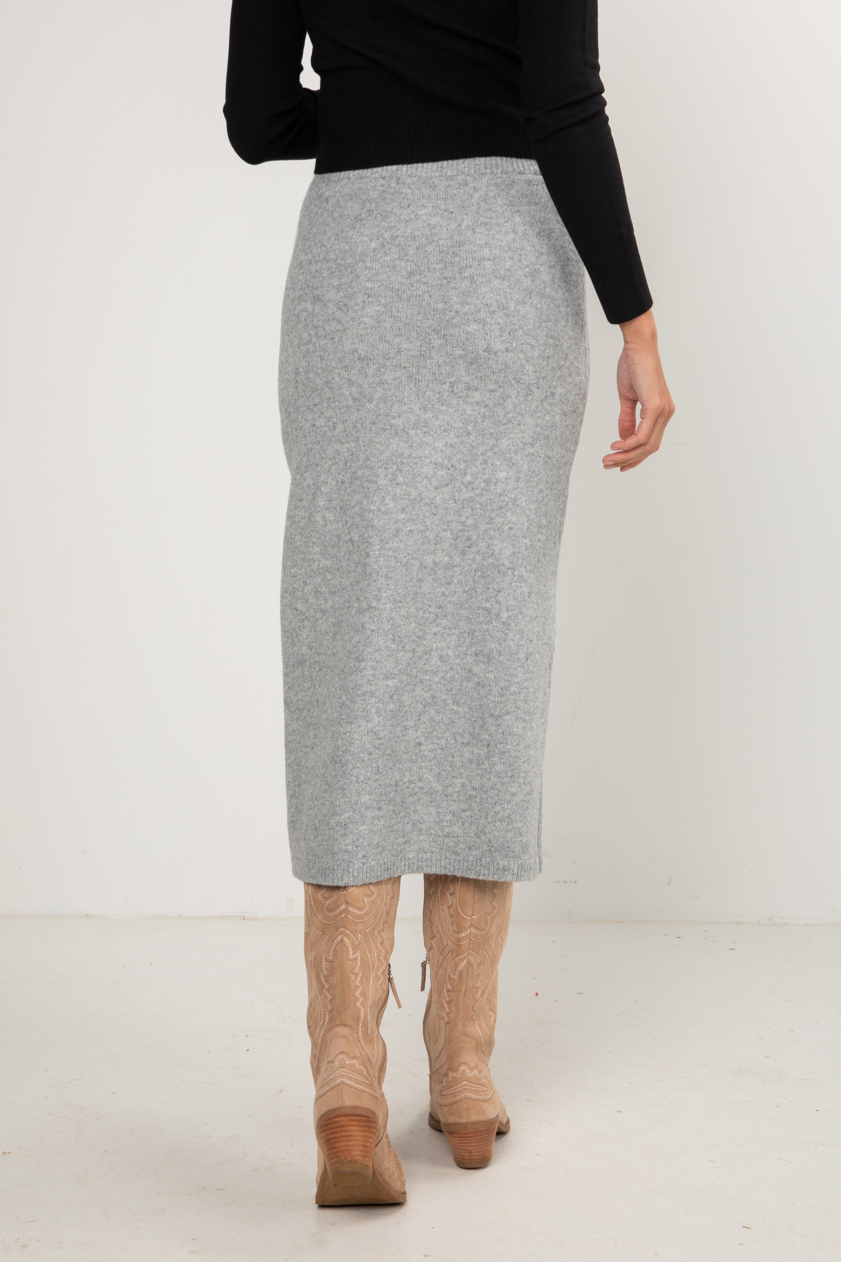 Woman wearing a black button-down cardigan and a grey knit midi skirt styled with tan cowboy boots.