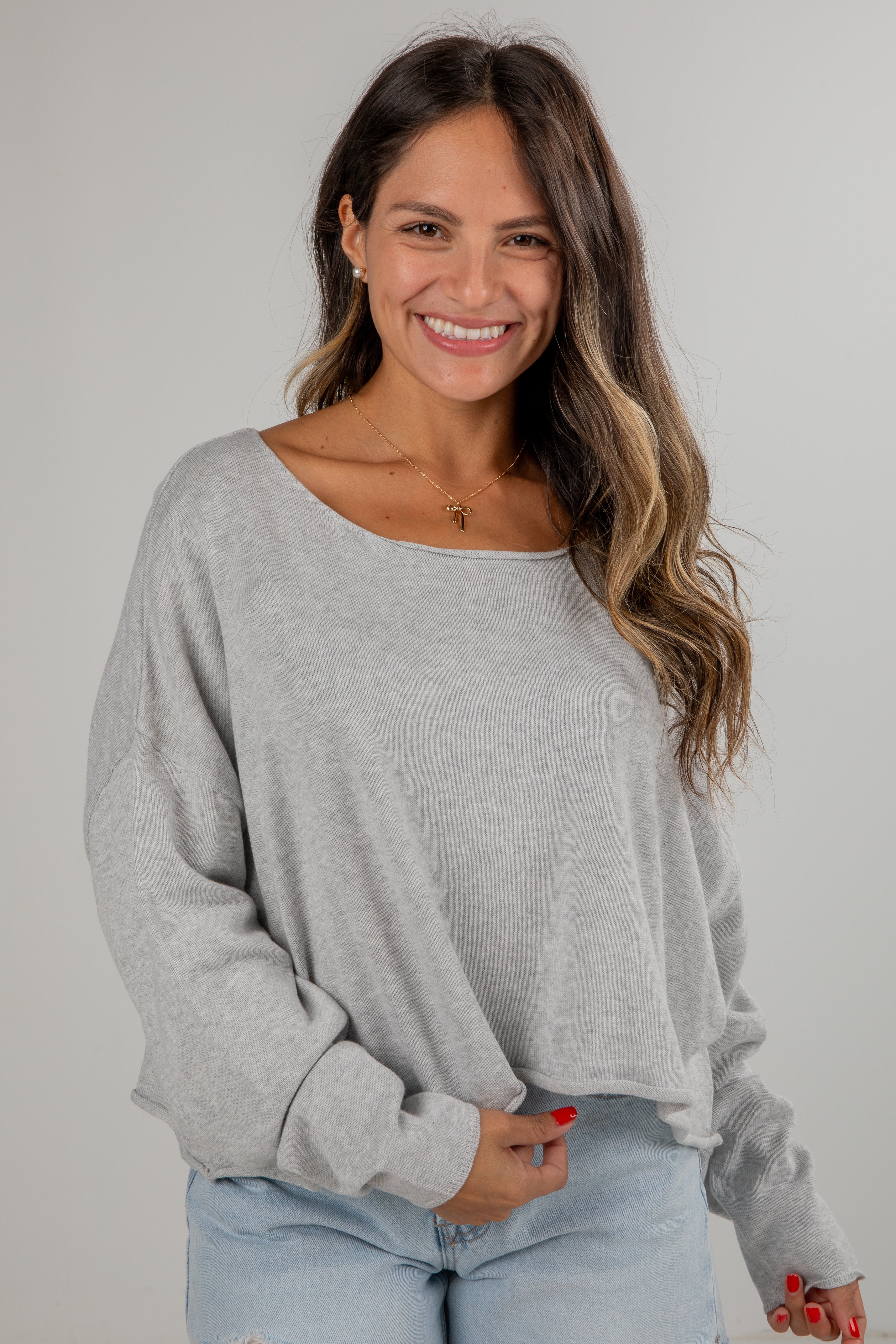 Woman wearing a gray sweater and light blue jeans against a plain background