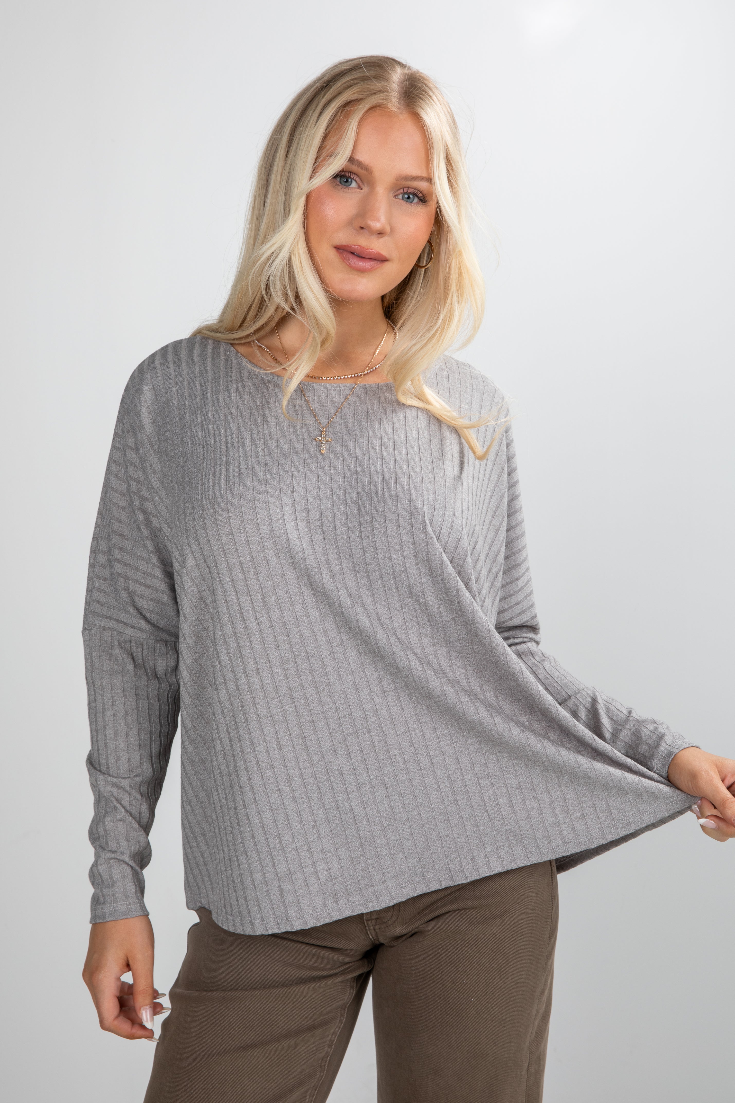 Woman wearing a gray ribbed sweater and brown pants against a white background