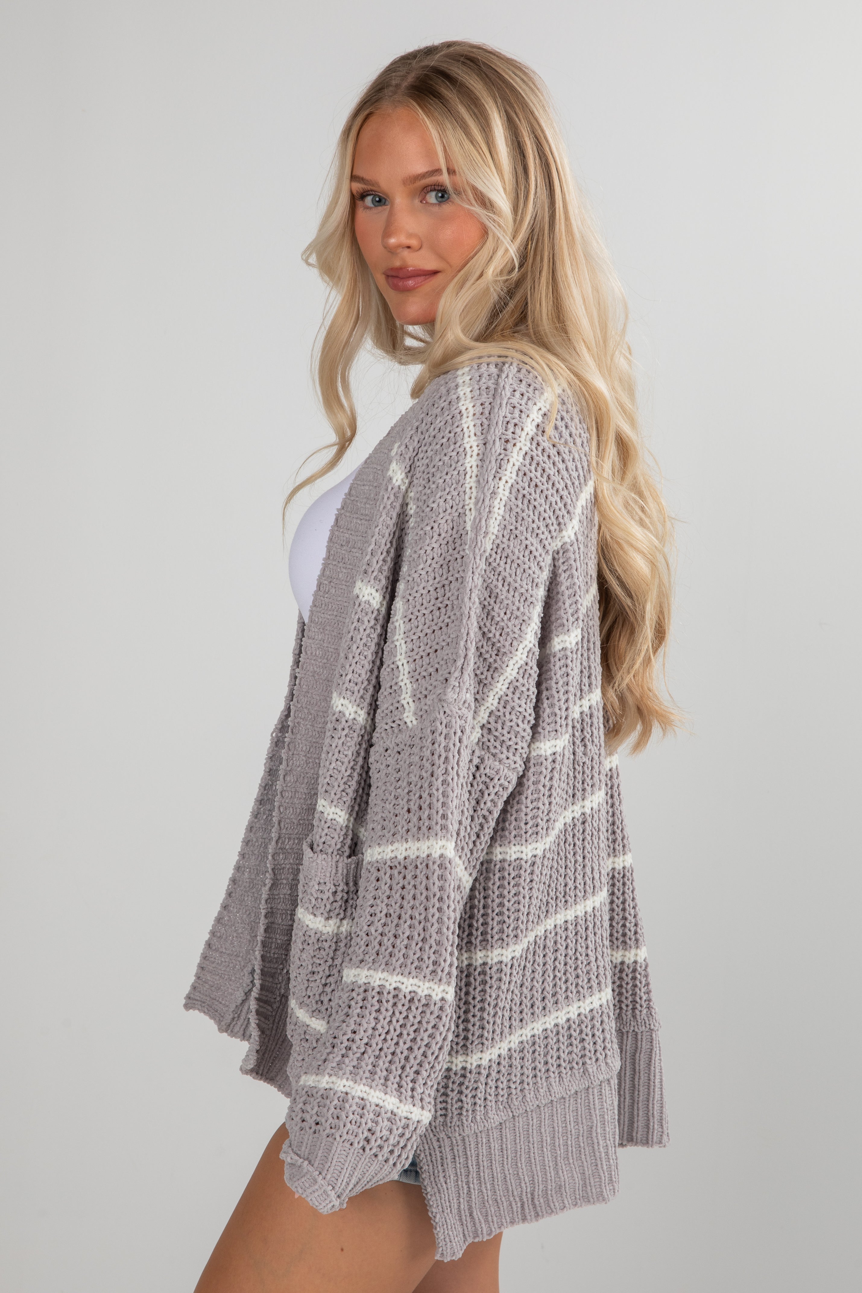 Woman wearing a gray knitted cardigan with white stripes on a plain background