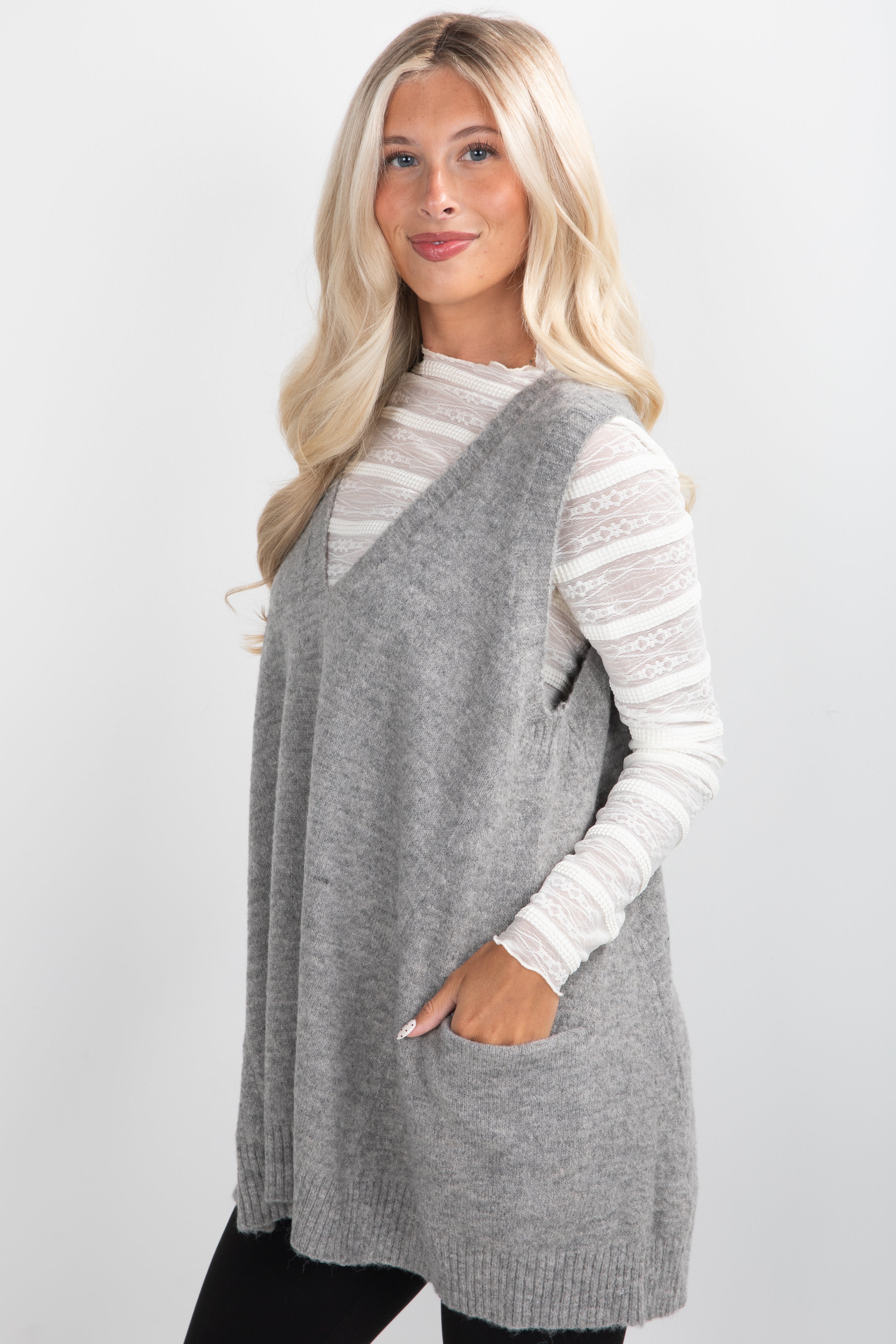 Woman wearing a gray knit vest over a white sweater on a plain background